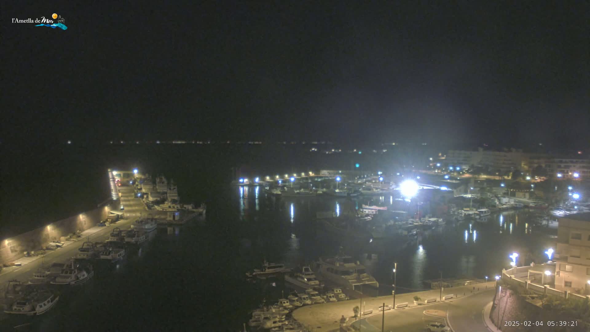 A nighttime, high-angle view of a harbor filled with boats, illuminated by lights from buildings and the boats themselves.