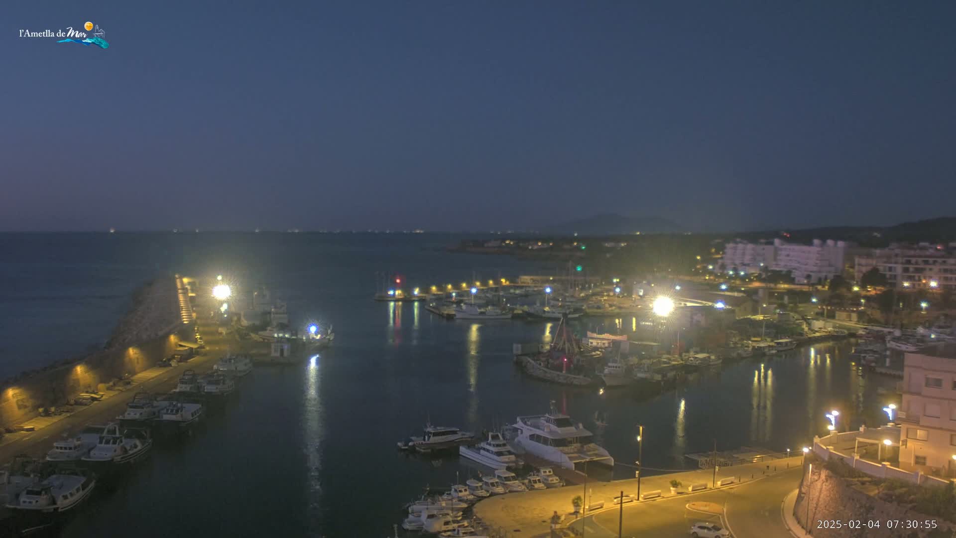 A nighttime view of a harbor filled with boats, illuminated by lights, under a dark sky.
