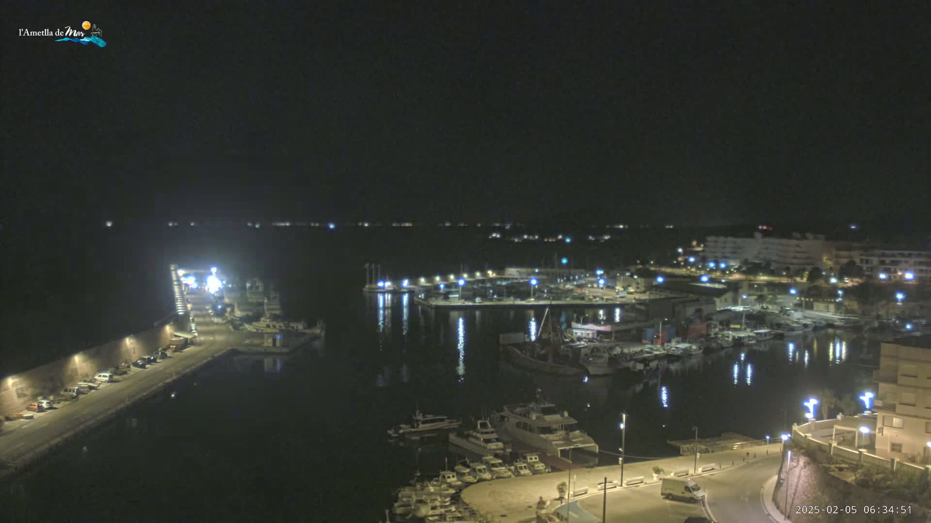 A nighttime view of a harbor filled with boats, illuminated by lights along the docks and buildings, under a clear, dark sky.