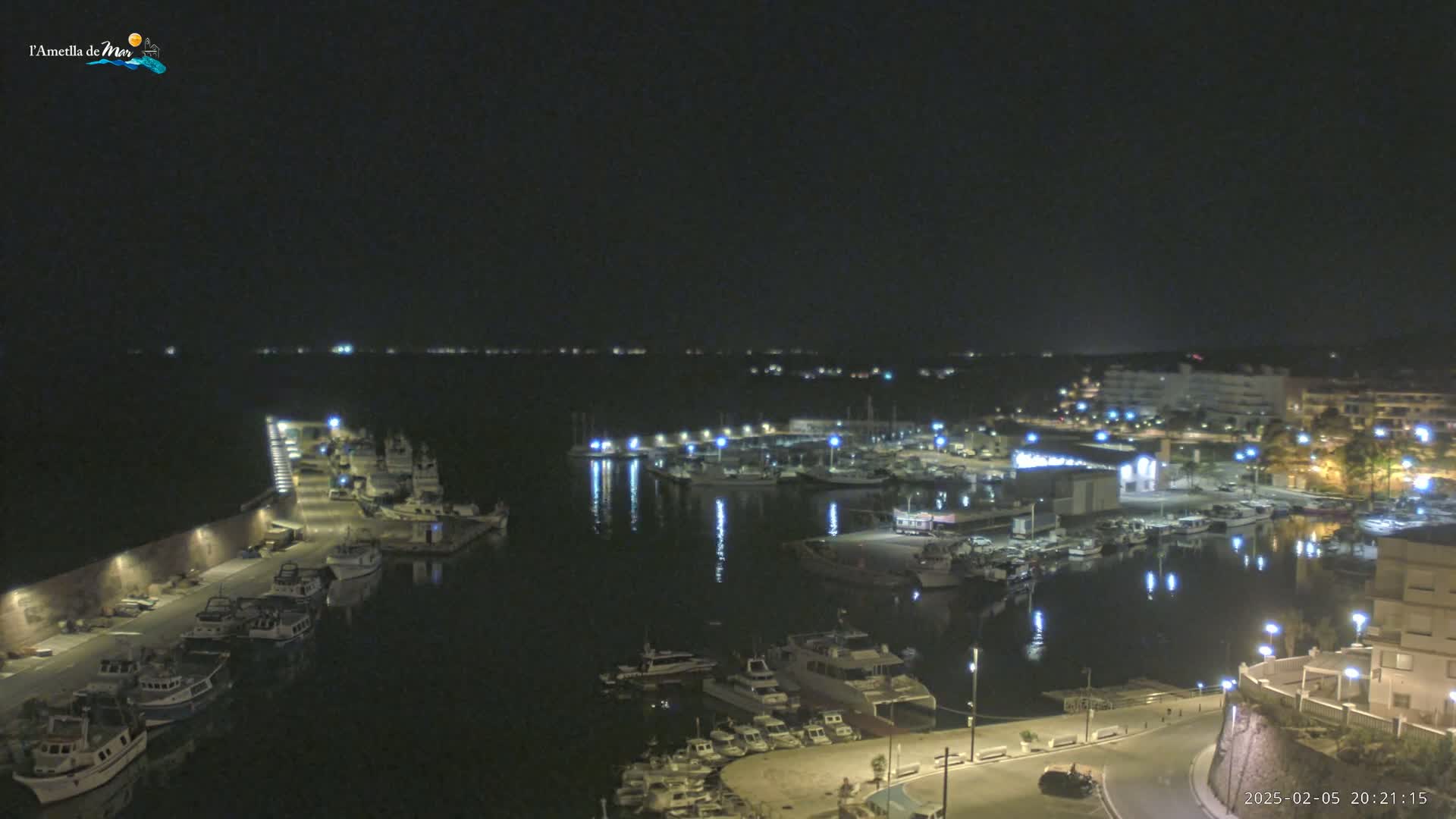 A nighttime view of a harbor filled with boats, lit by streetlights and the reflections of lights on the water.
