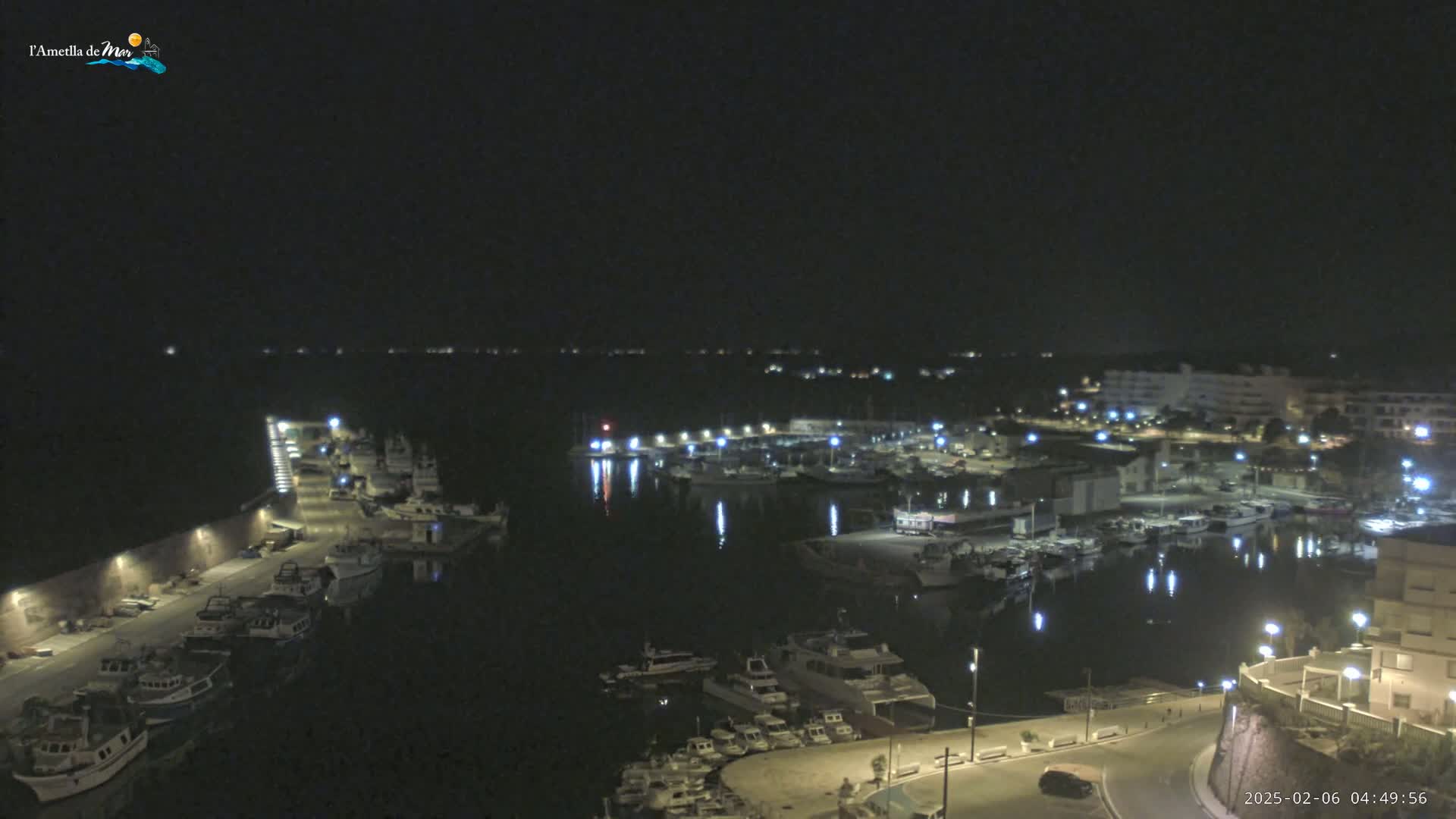 A nighttime aerial view of a harbor filled with boats, illuminated by lights along the docks and buildings surrounding the water.