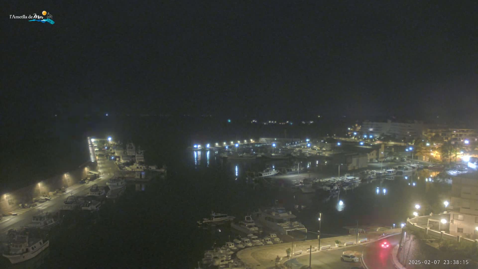 A nighttime, aerial view of a harbor filled with boats, surrounded by buildings and illuminated by streetlights.