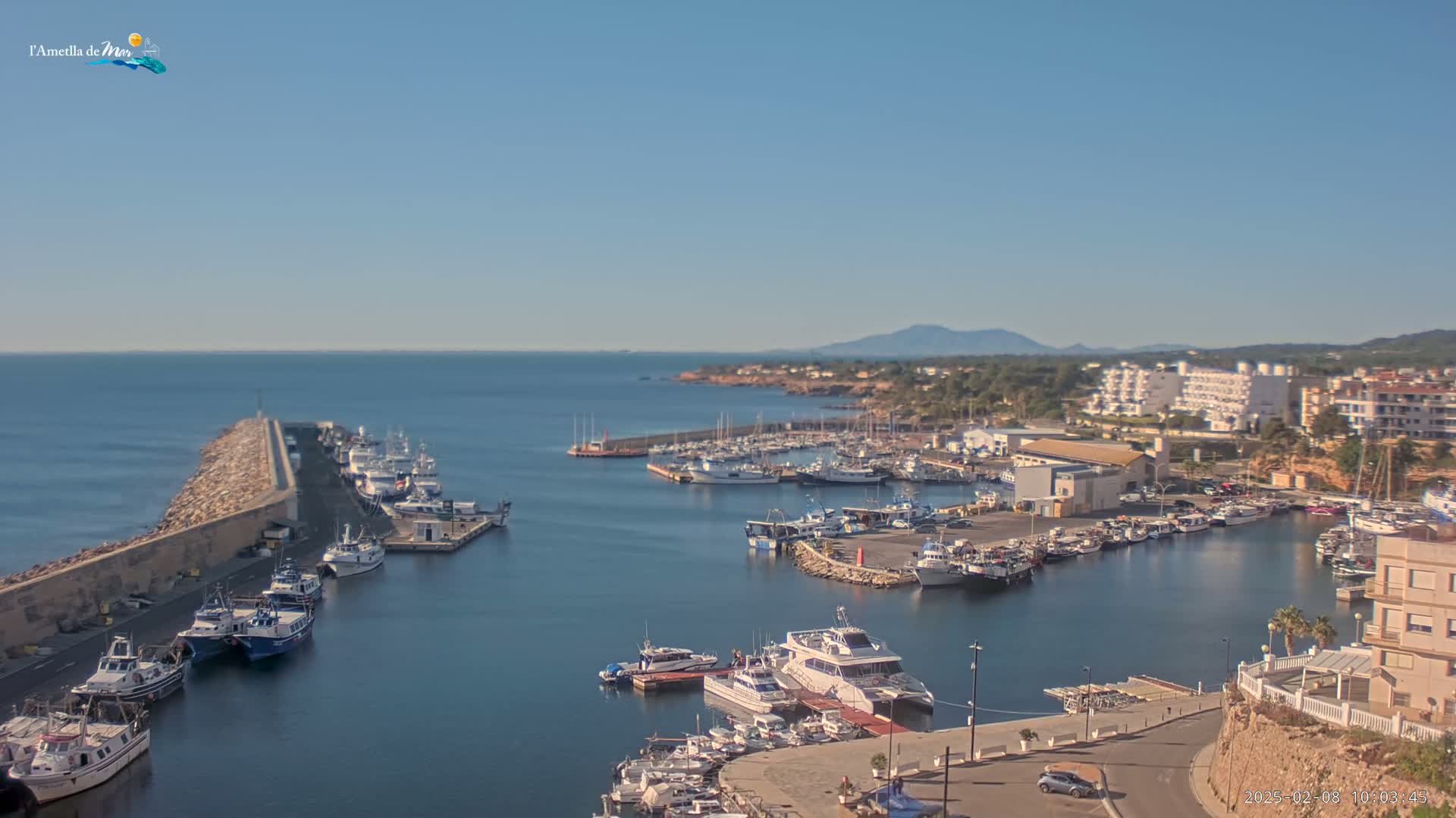 A harbor filled with numerous boats and yachts is situated next to a coastal town under a clear, sunny sky.