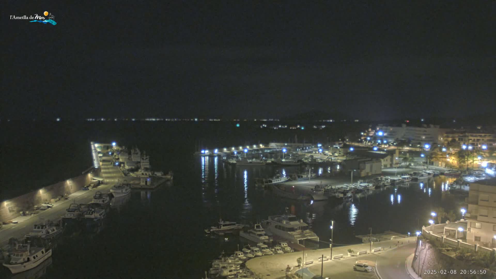A nighttime, high-angle view of a harbor filled with boats, illuminated by lights along the docks and buildings surrounding the water.