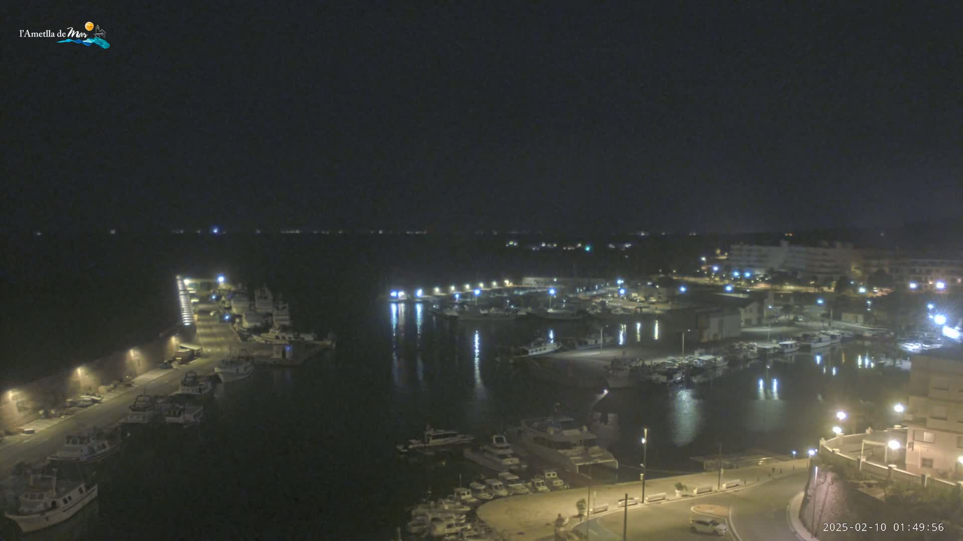 A nighttime, high-angle view of a harbor filled with boats, illuminated by streetlights and building lights, under a clear, dark sky.