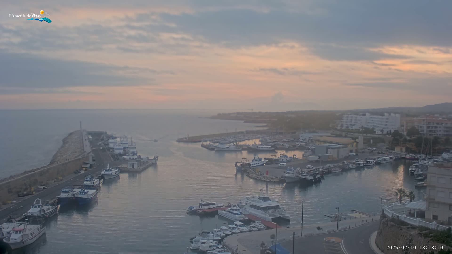 A harbor filled with numerous boats is seen at sunrise under a hazy, pinkish sky.