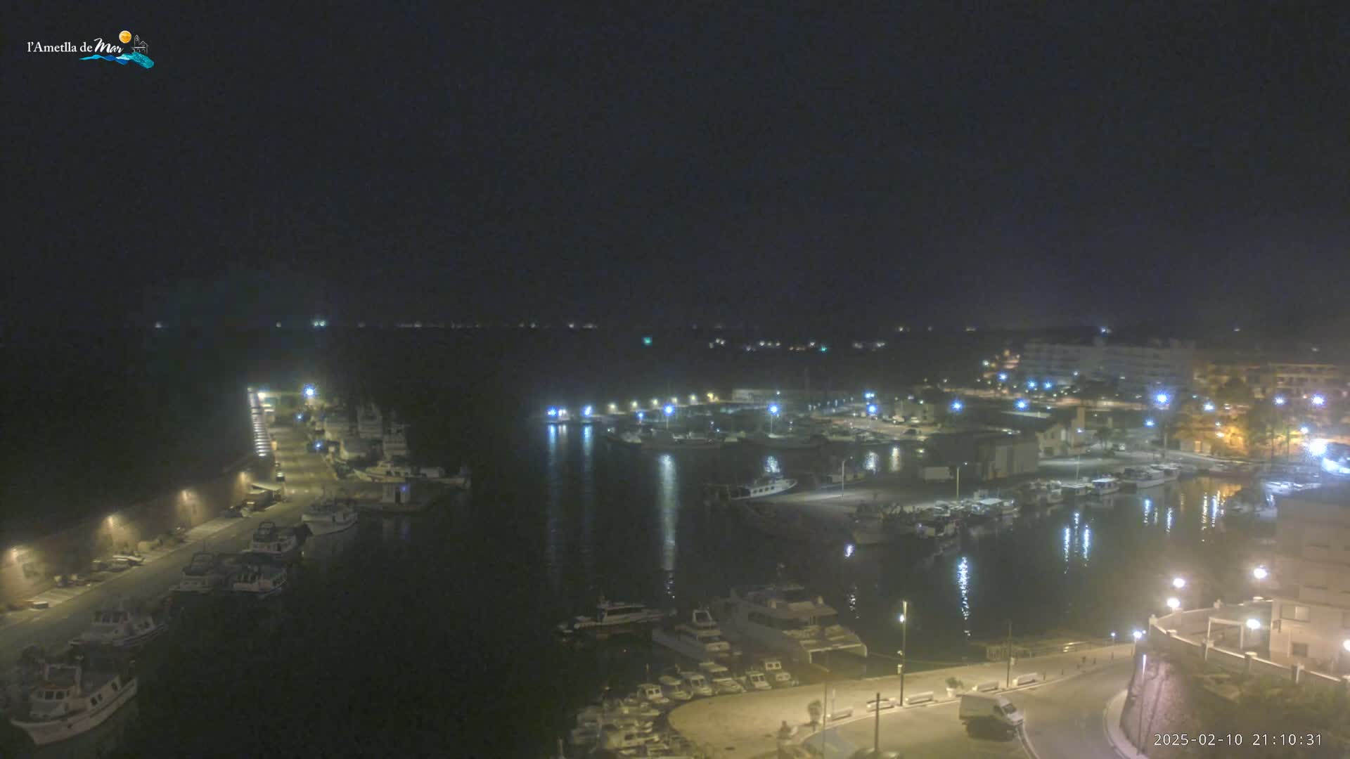 A nighttime aerial view of a harbor filled with boats, surrounded by buildings with lights on under a clear, dark sky.