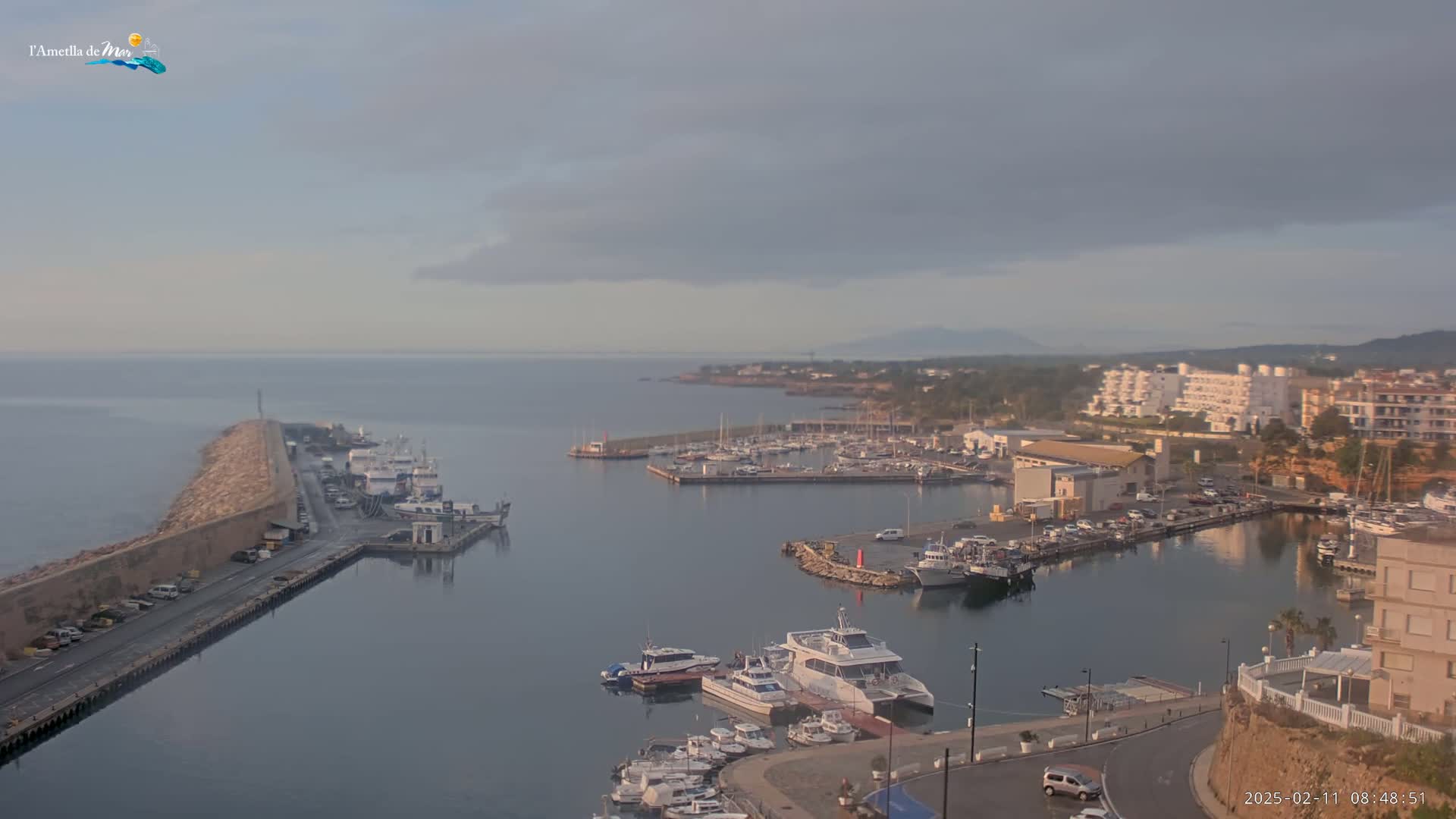 An overcast day reveals a harbor filled with boats, a breakwater, and coastal buildings.