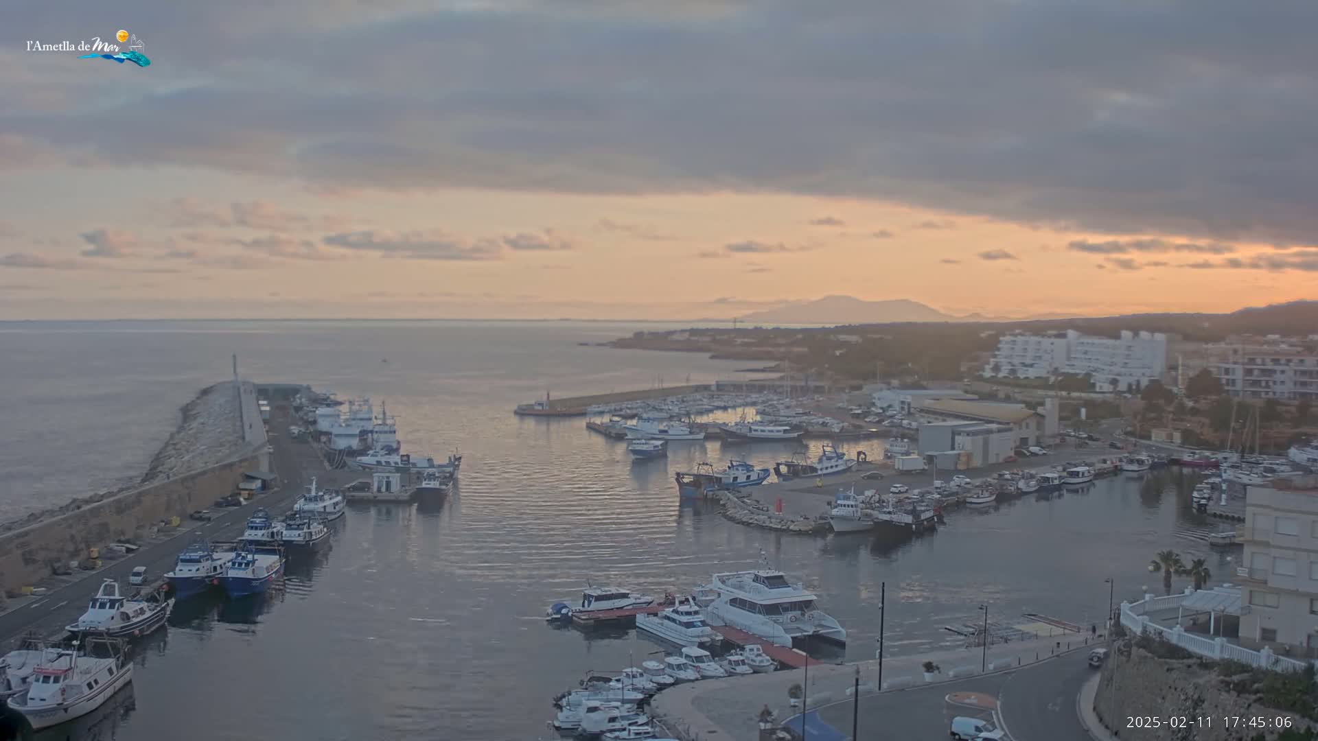 A harbor filled with numerous boats is seen at sunset under a partly cloudy sky.