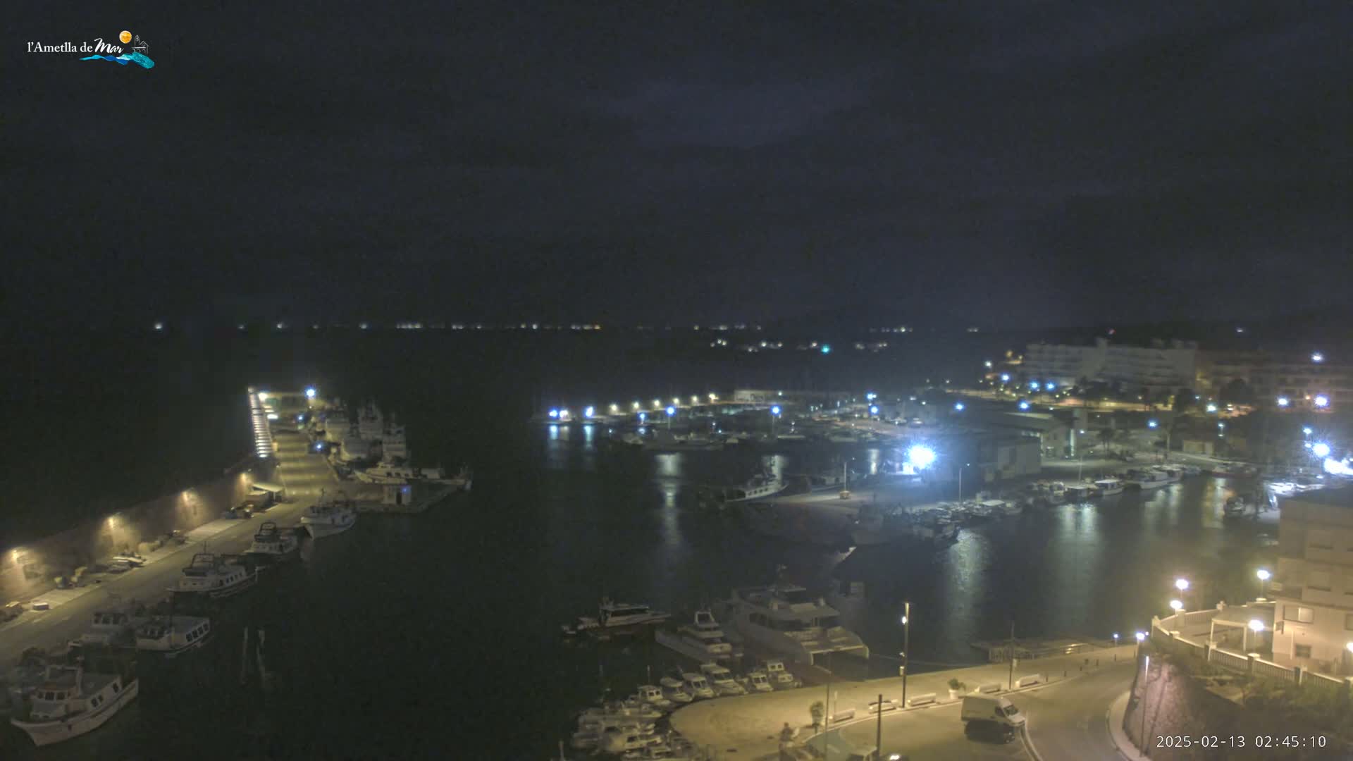 A nighttime, aerial view of a harbor filled with boats, illuminated by lights, under a dark, cloudy sky.