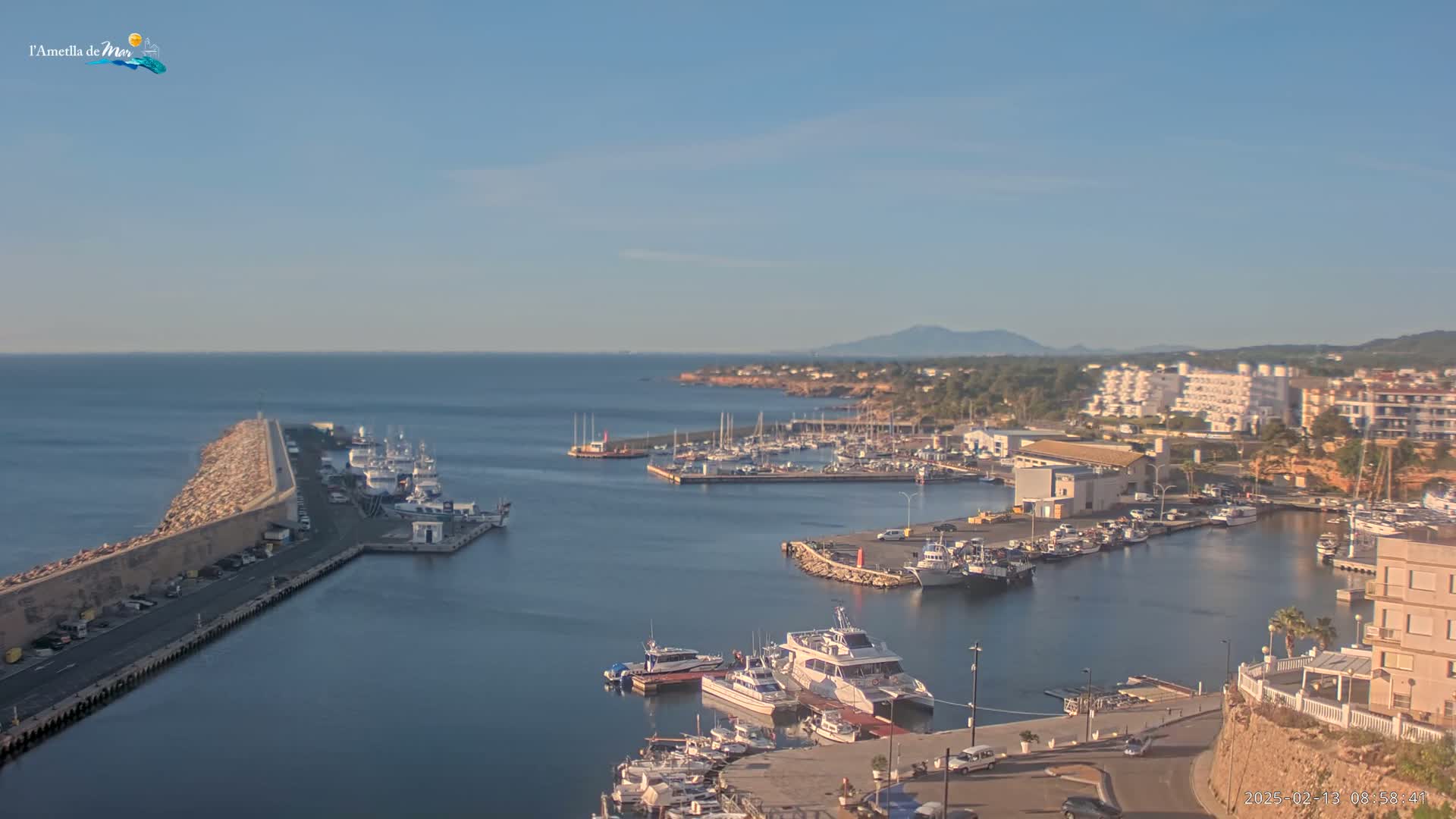 A harbor filled with boats and surrounded by buildings is seen on a clear, sunny day.