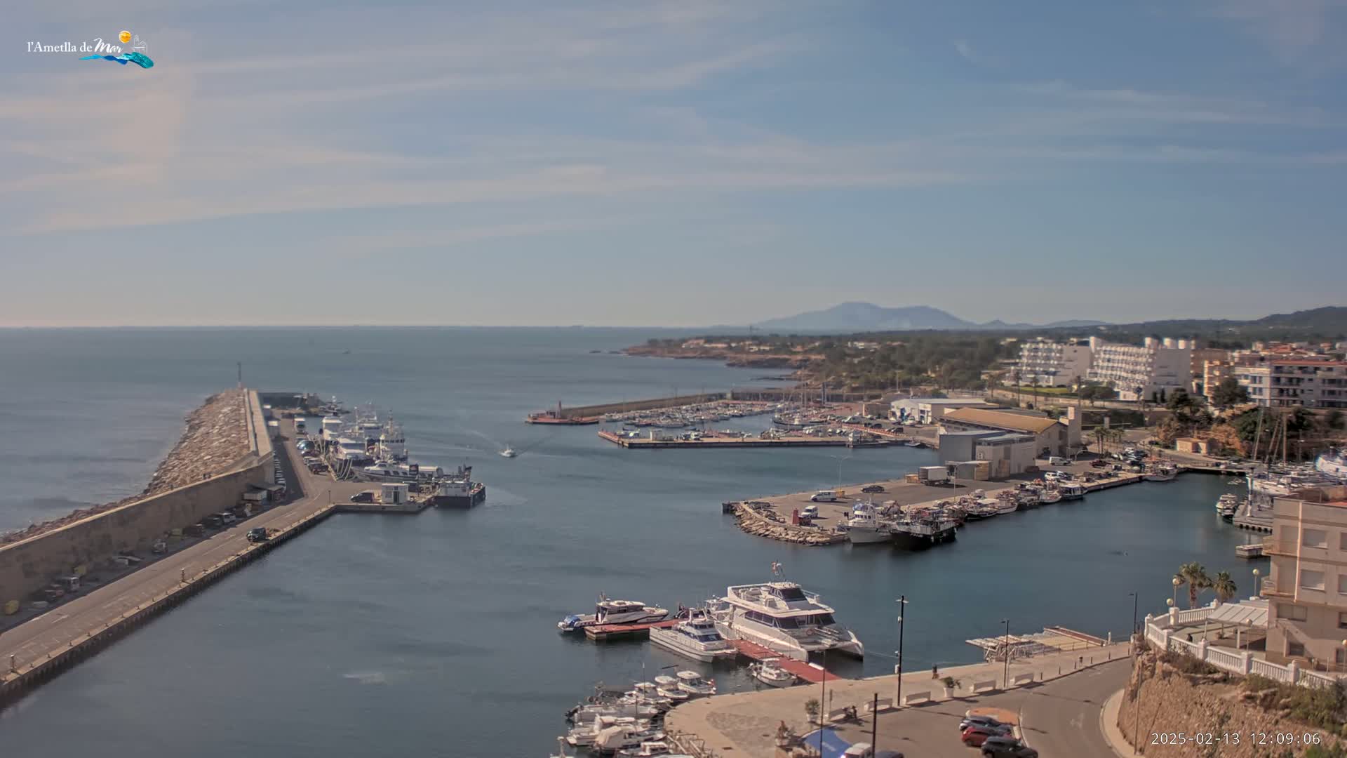 A harbor filled with boats and surrounded by buildings and a rocky coastline under a mostly clear sky.