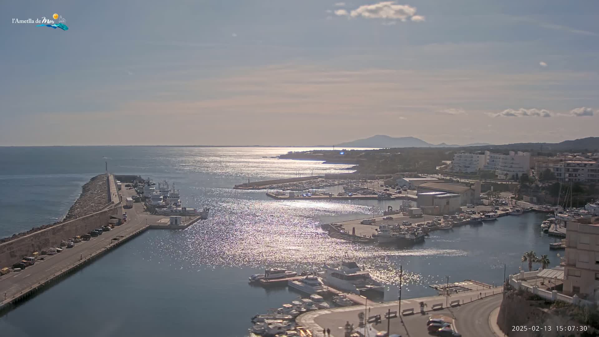A harbor filled with boats is seen from an elevated viewpoint on a sunny day with a few clouds in the sky.