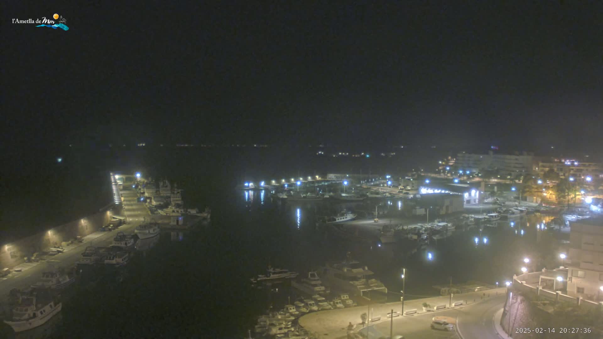 A nighttime, aerial view of a harbor filled with boats, docked along a shoreline with buildings and streetlights.