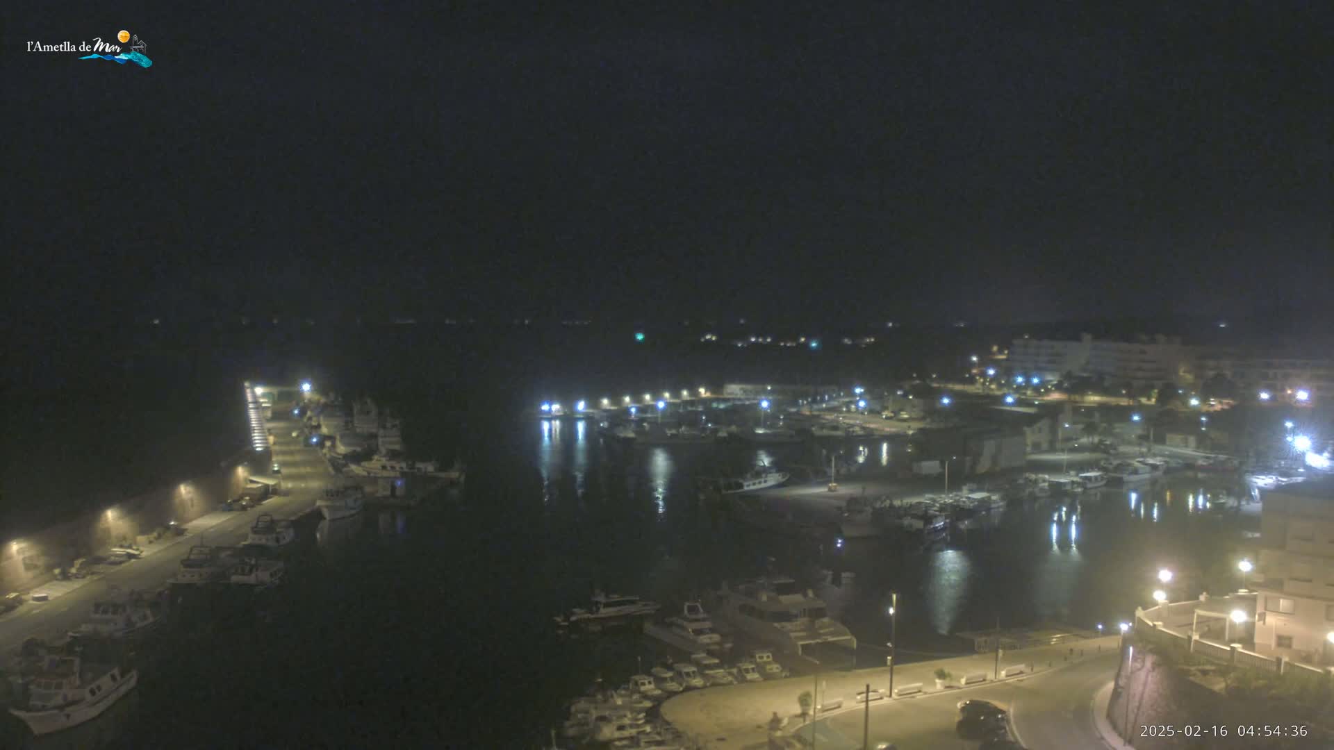 A nighttime aerial view of a harbor filled with boats, illuminated by streetlights and building lights under a dark sky.