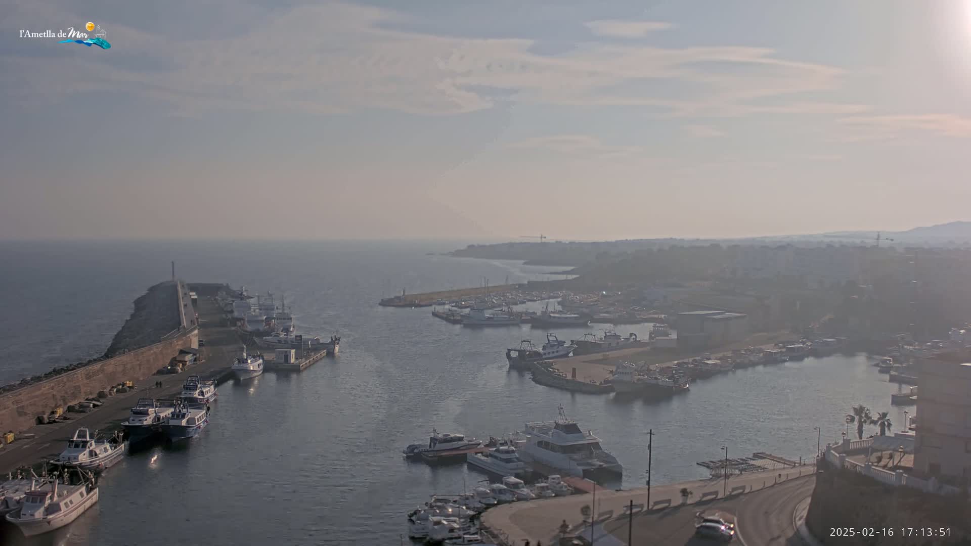 A hazy harbor filled with numerous boats and ships, a stone breakwater extending into the sea.