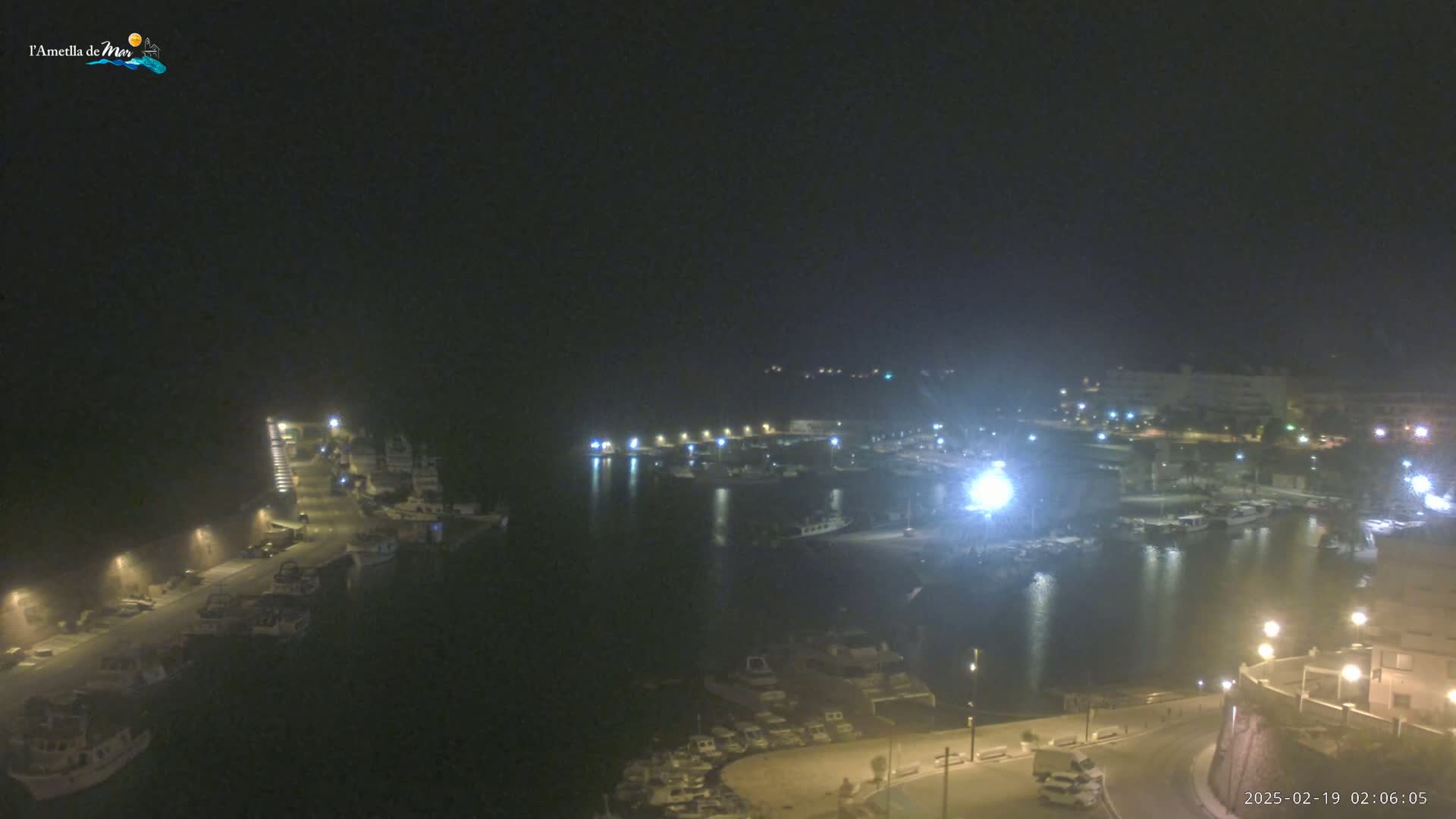 A nighttime, high-angle view of a harbor filled with boats, illuminated by streetlights and building lights.
