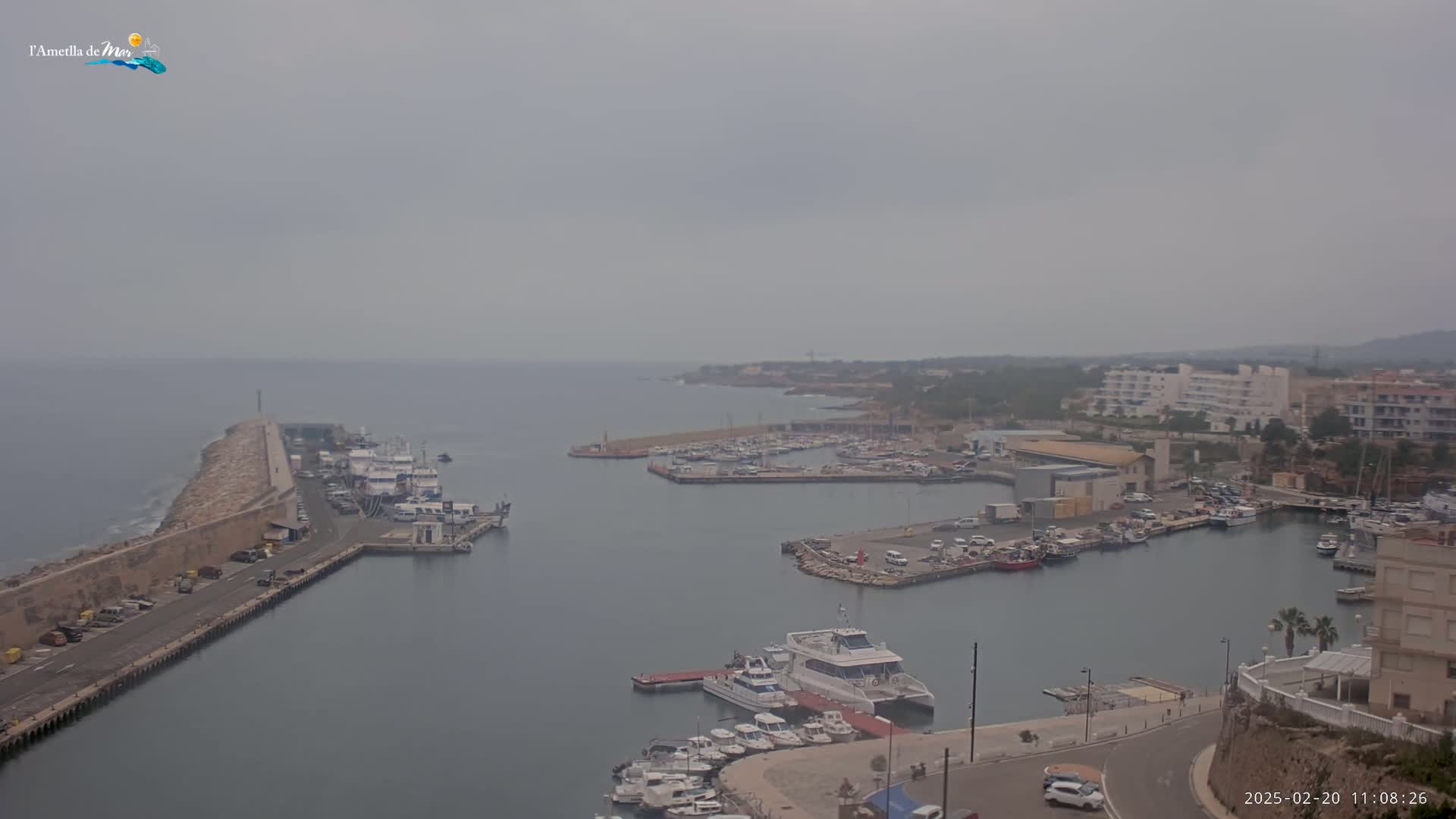 A hazy day reveals a harbor filled with boats and buildings, with a long stone breakwater extending into the sea.