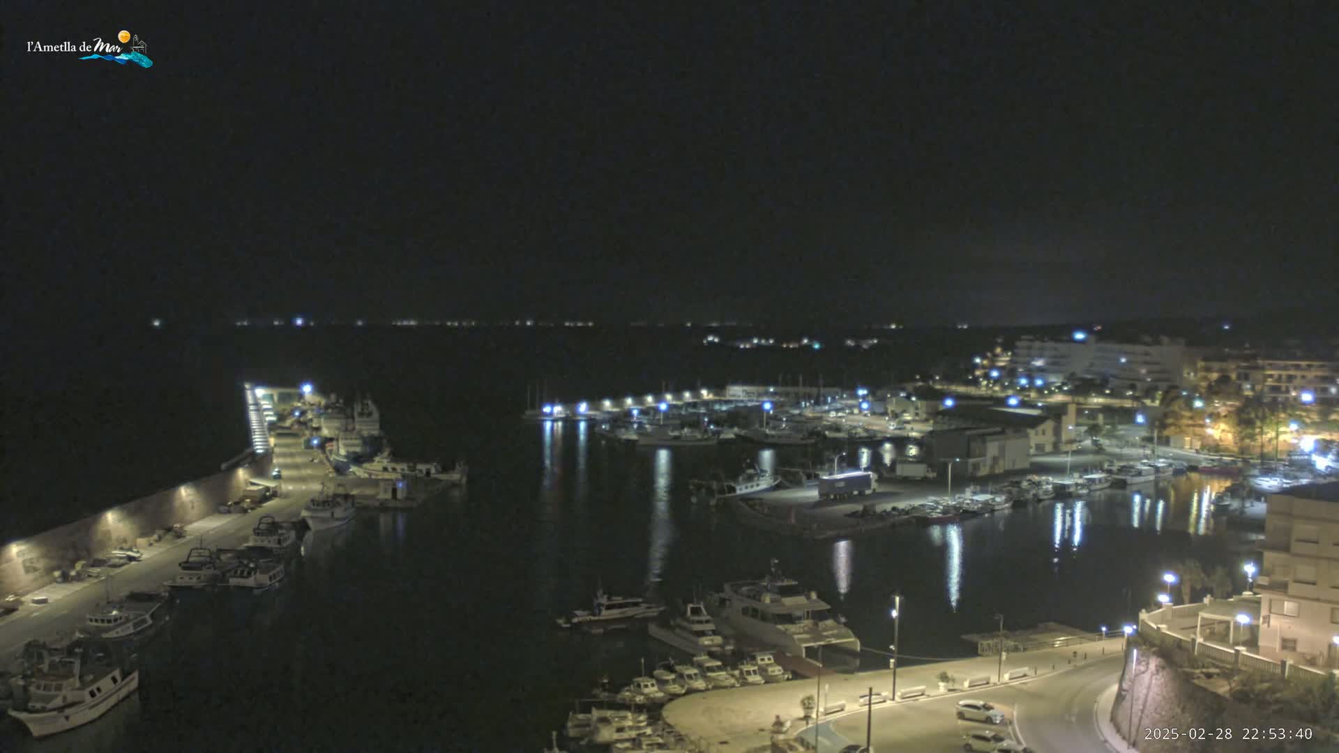 A nighttime, high-angle view of a harbor filled with boats, illuminated by lights along the docks and surrounding buildings.