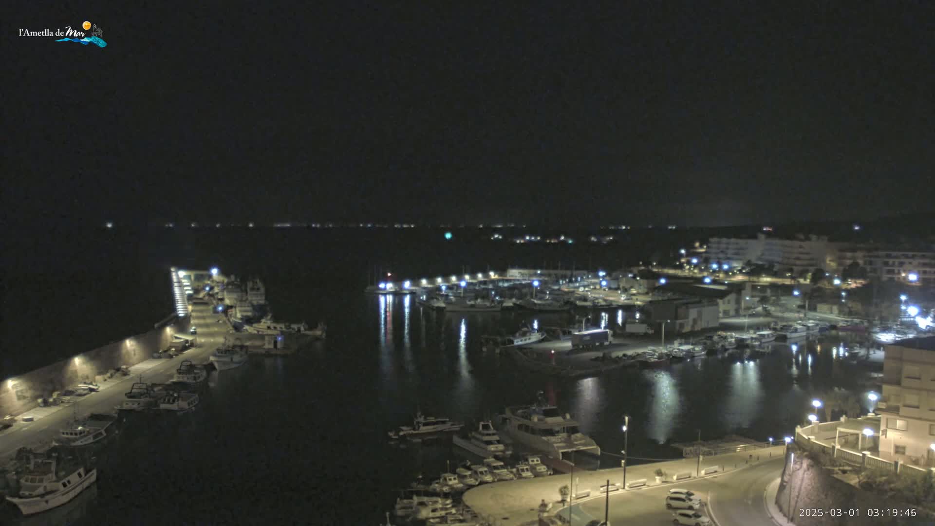 A nighttime aerial view of a harbor filled with boats, illuminated by lights along the waterfront and buildings beyond.