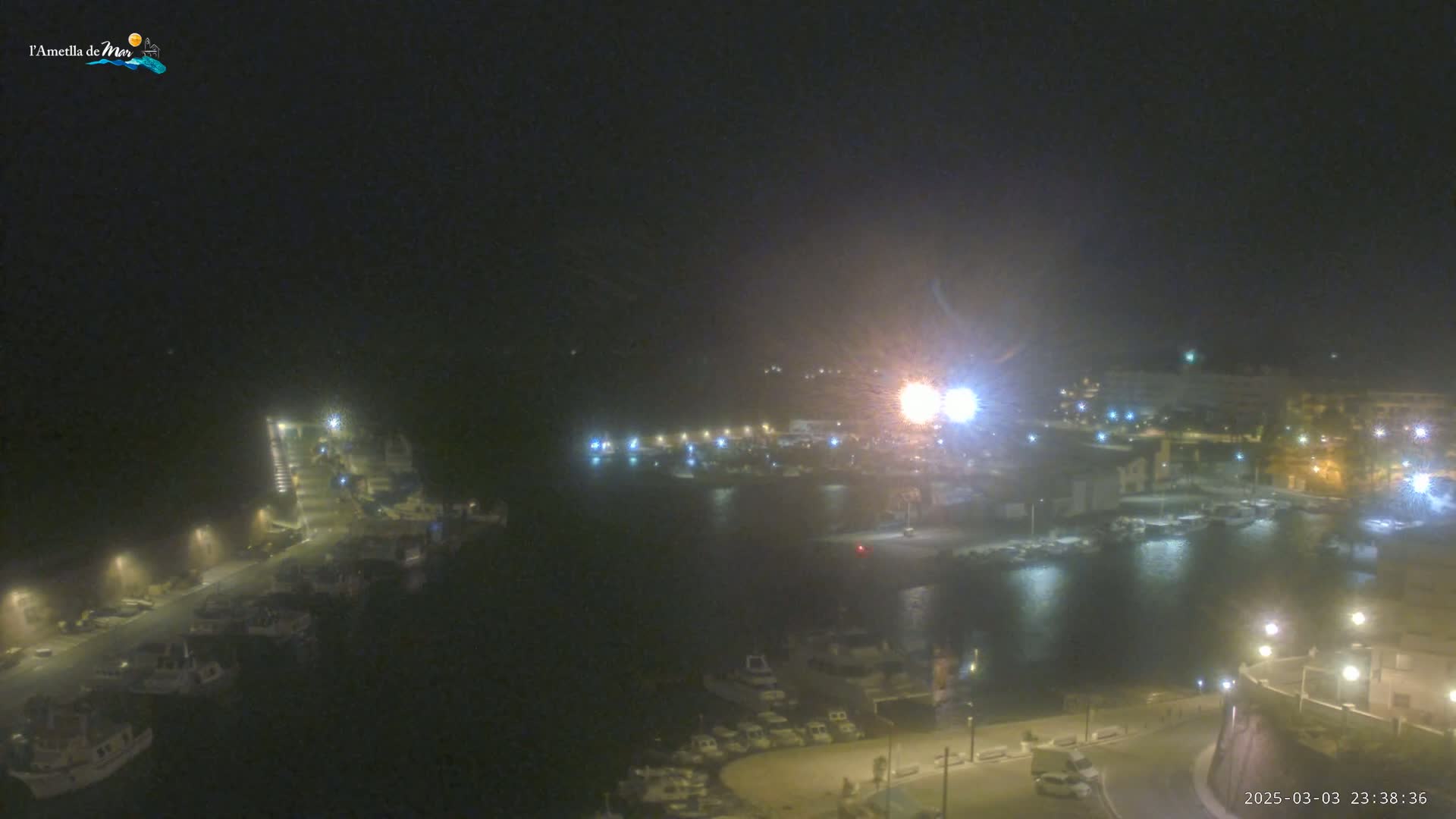 A nighttime, hazy view of a harbor filled with boats, illuminated by streetlights and other artificial light sources.