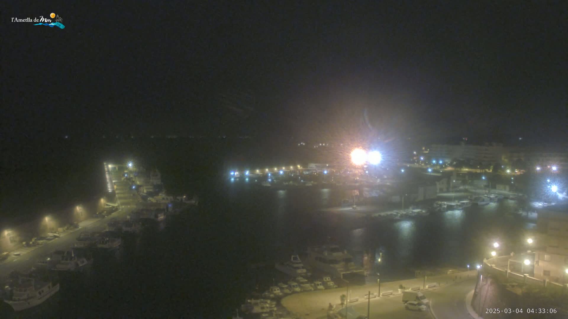 A nighttime, hazy view of a harbor filled with boats, illuminated by streetlights and other lights along the waterfront.