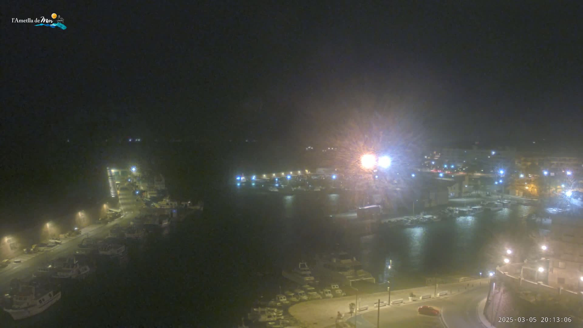 A nighttime view of a harbor filled with boats, under hazy or snowy conditions, with buildings and lights illuminating the scene.