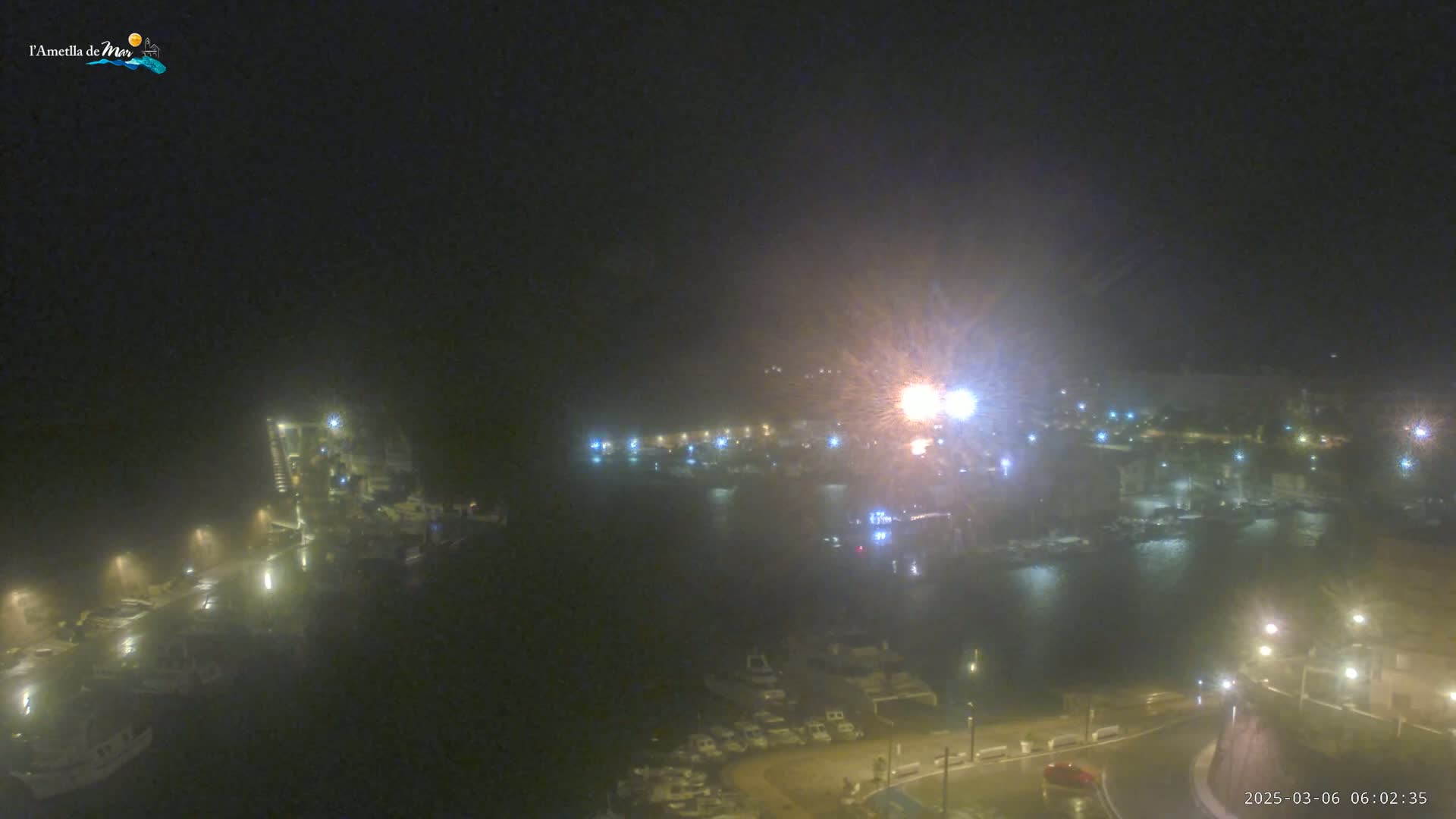 A nighttime harbor scene with hazy or foggy conditions shows many boats moored along a waterfront, illuminated by various lights.