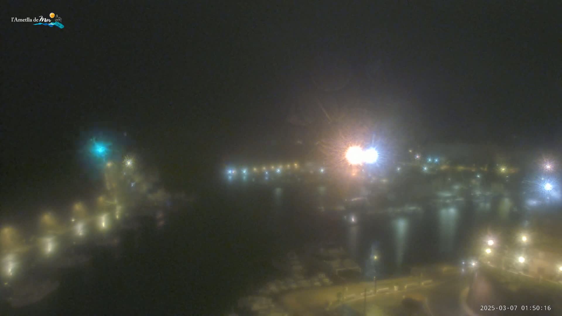 A foggy, nighttime view of a harbor with numerous lights reflecting on the water.