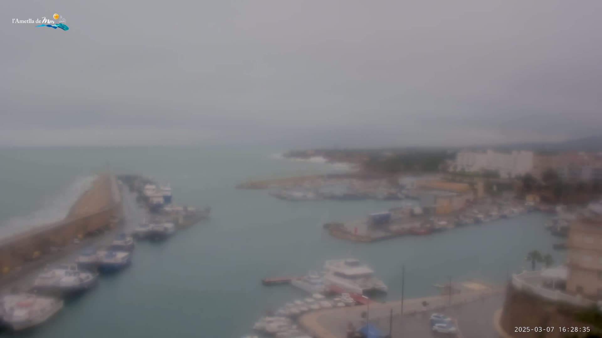 A hazy, overcast day reveals a harbor filled with numerous boats and surrounded by buildings, with a breakwater extending into the sea.
