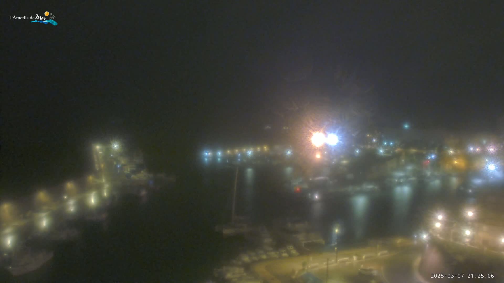 A nighttime, foggy view of a harbor with many boats and lights reflecting on the water.