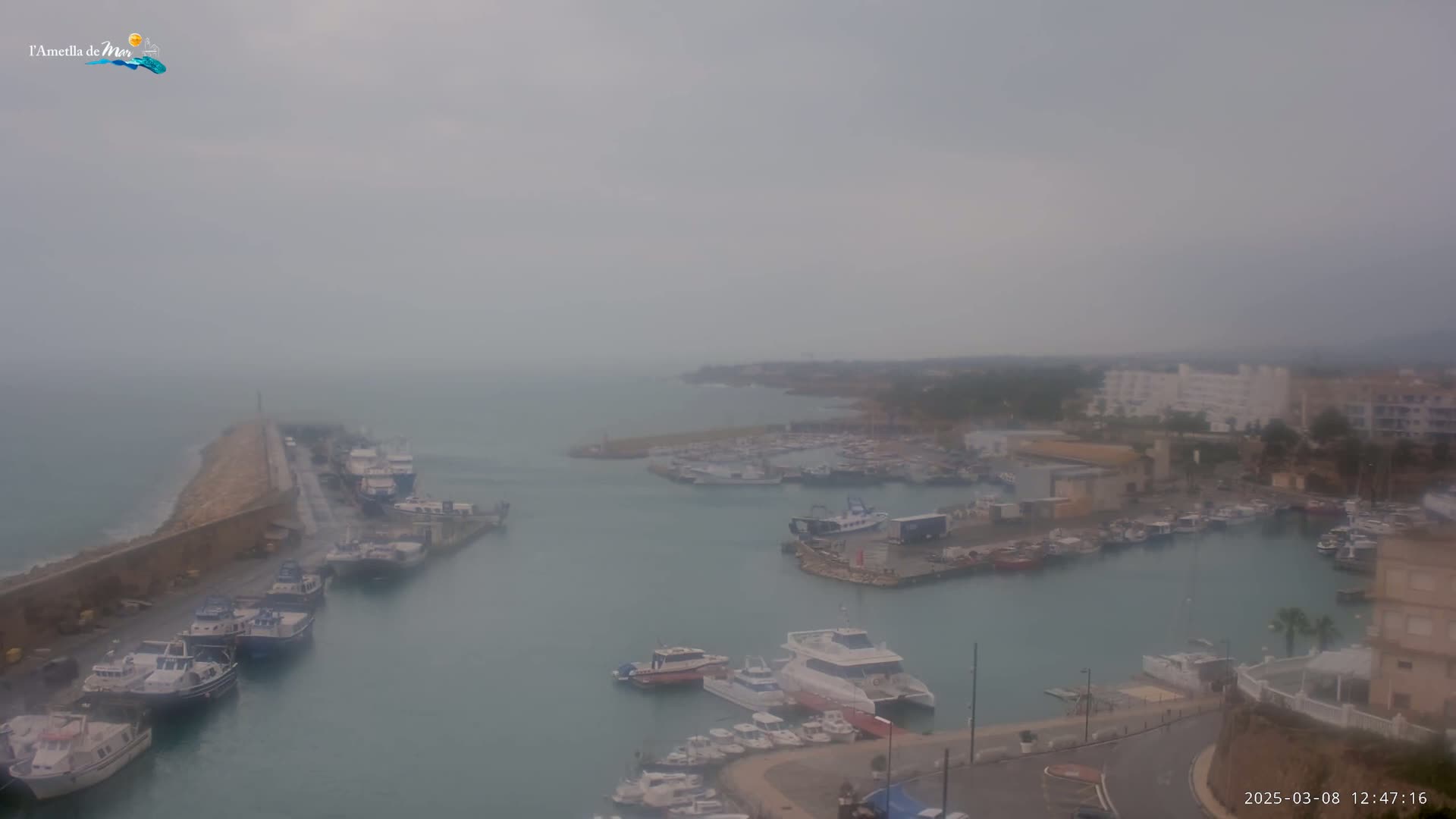 A hazy, overcast day reveals a harbor filled with numerous boats and ships, partially sheltered by a long stone breakwater.