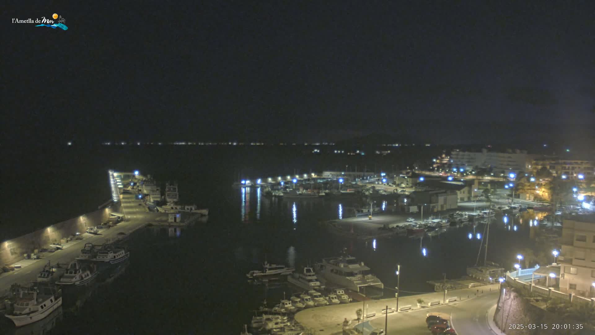 A nighttime, aerial view of a harbor filled with boats, with calm water reflecting the lights from the docked vessels and surrounding buildings.