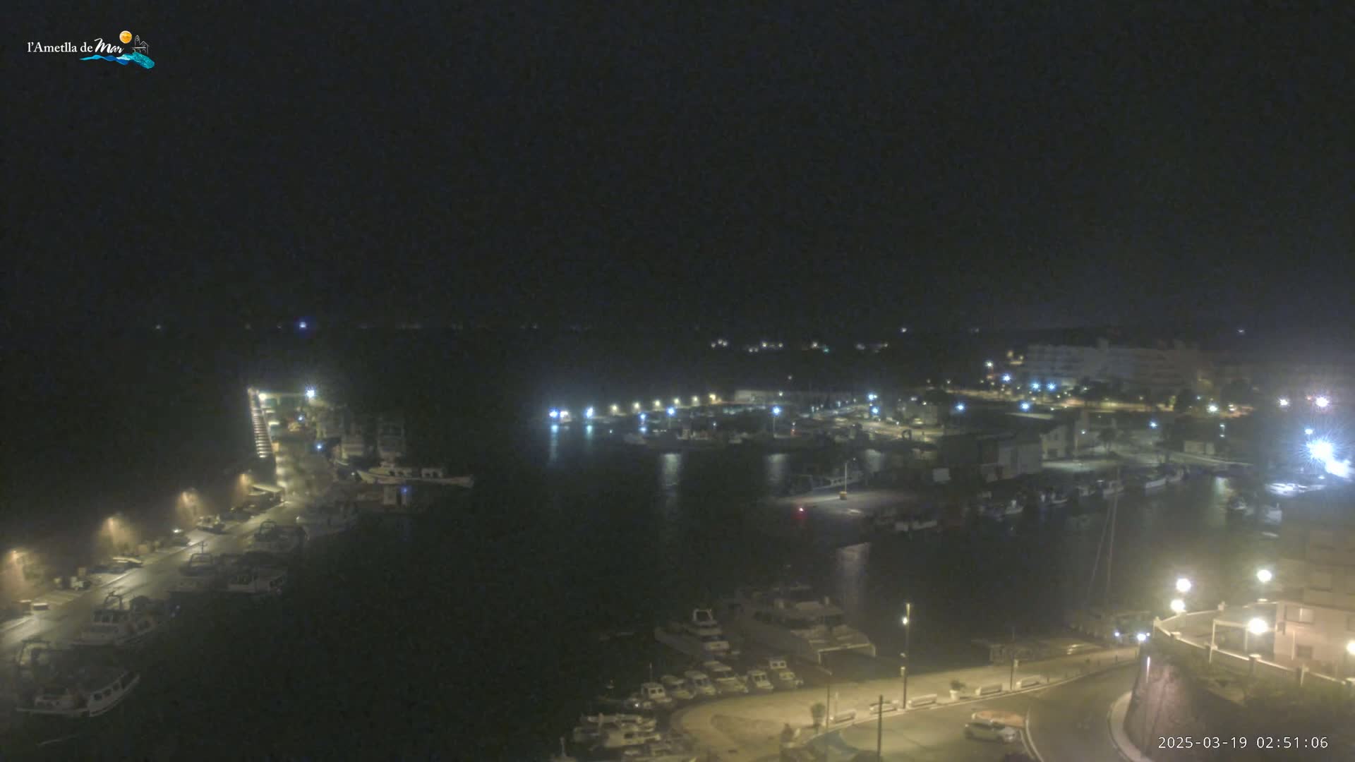 A nighttime, high-angle view of a harbor filled with boats, illuminated by streetlights and the glow of buildings on the shore.