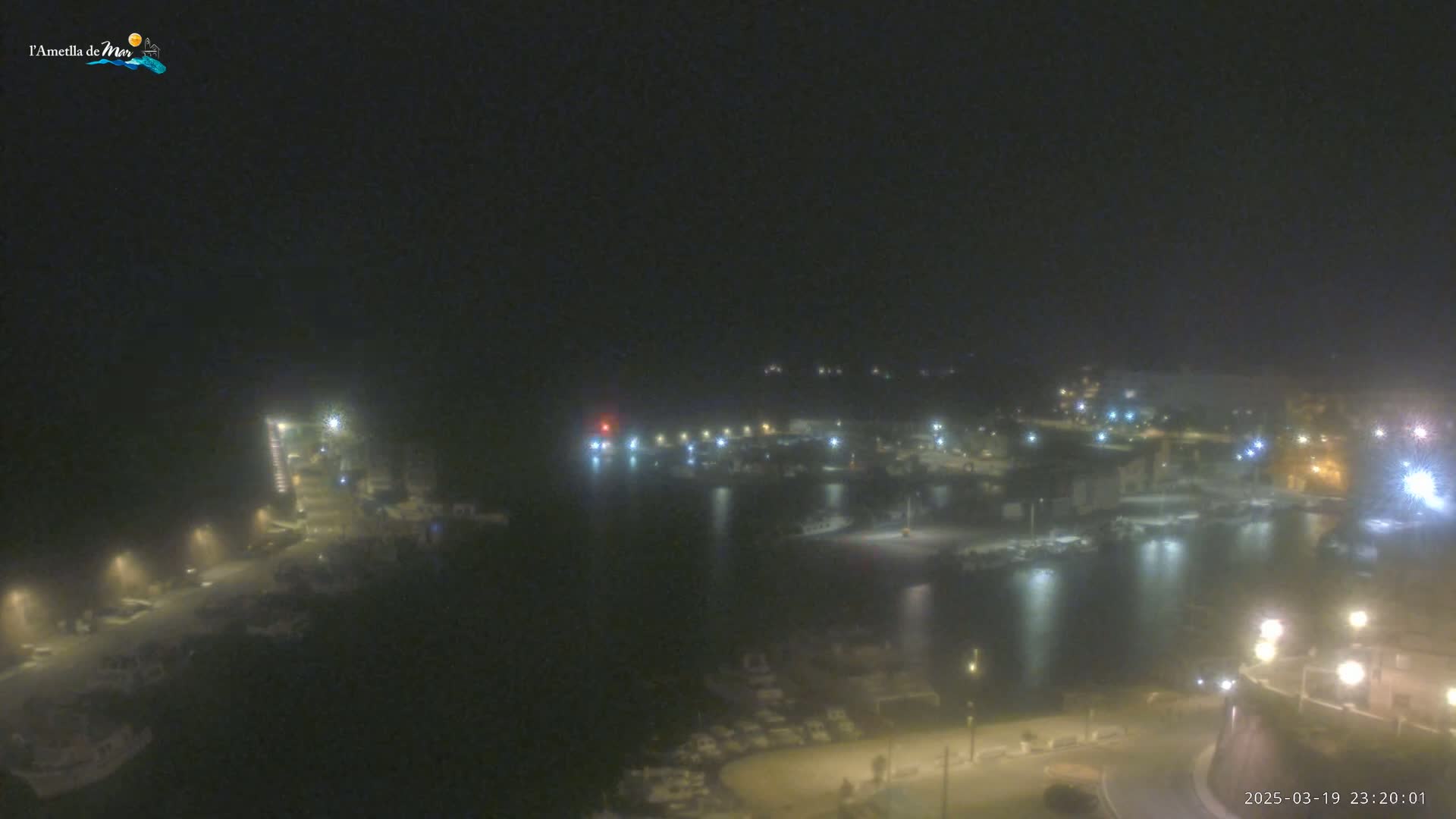 A nighttime view of a harbor filled with boats, under hazy or foggy conditions.