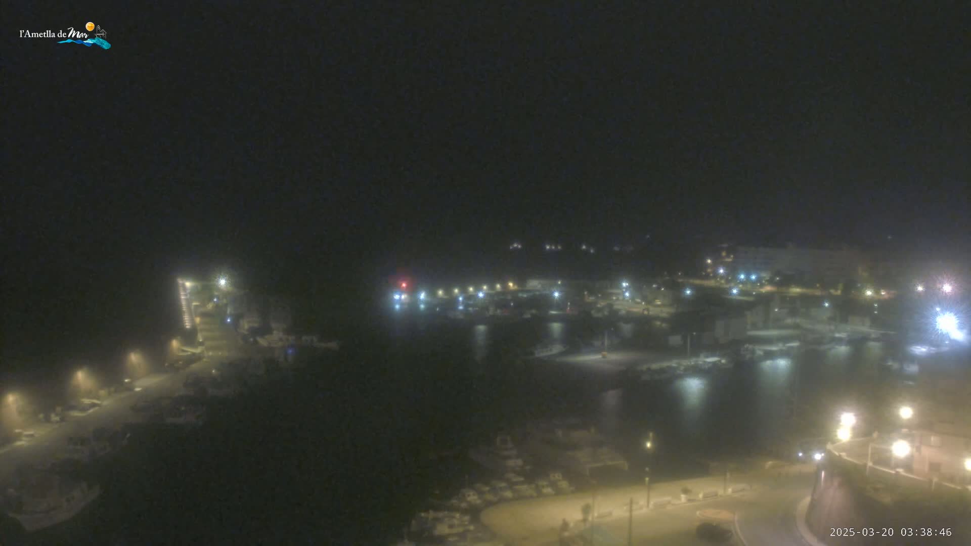 A nighttime, hazy view of a harbor filled with boats, illuminated by streetlights and the lights of buildings along the shoreline.