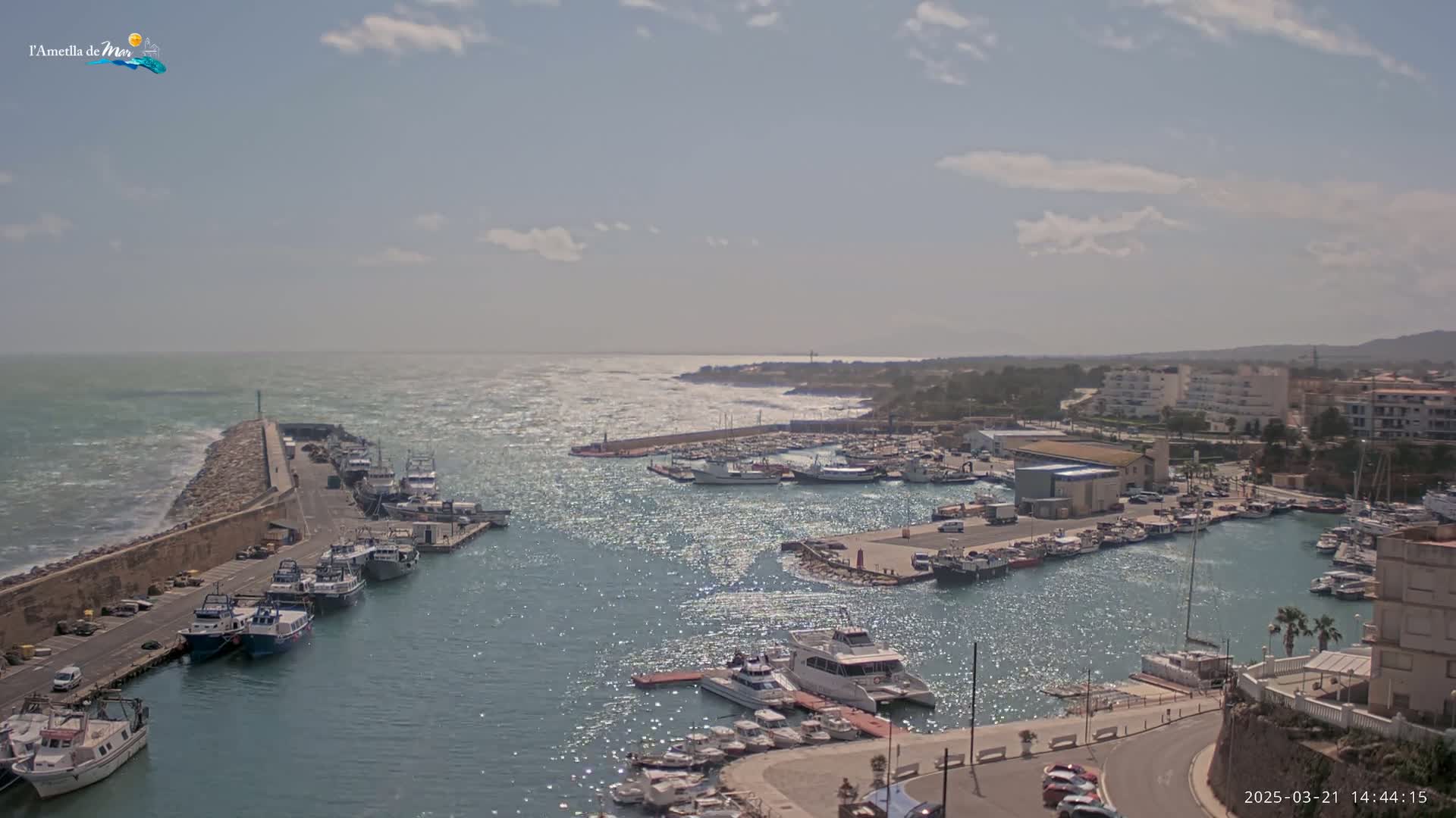A harbor filled with boats is seen from an elevated vantage point on a partly sunny day with a choppy sea.
