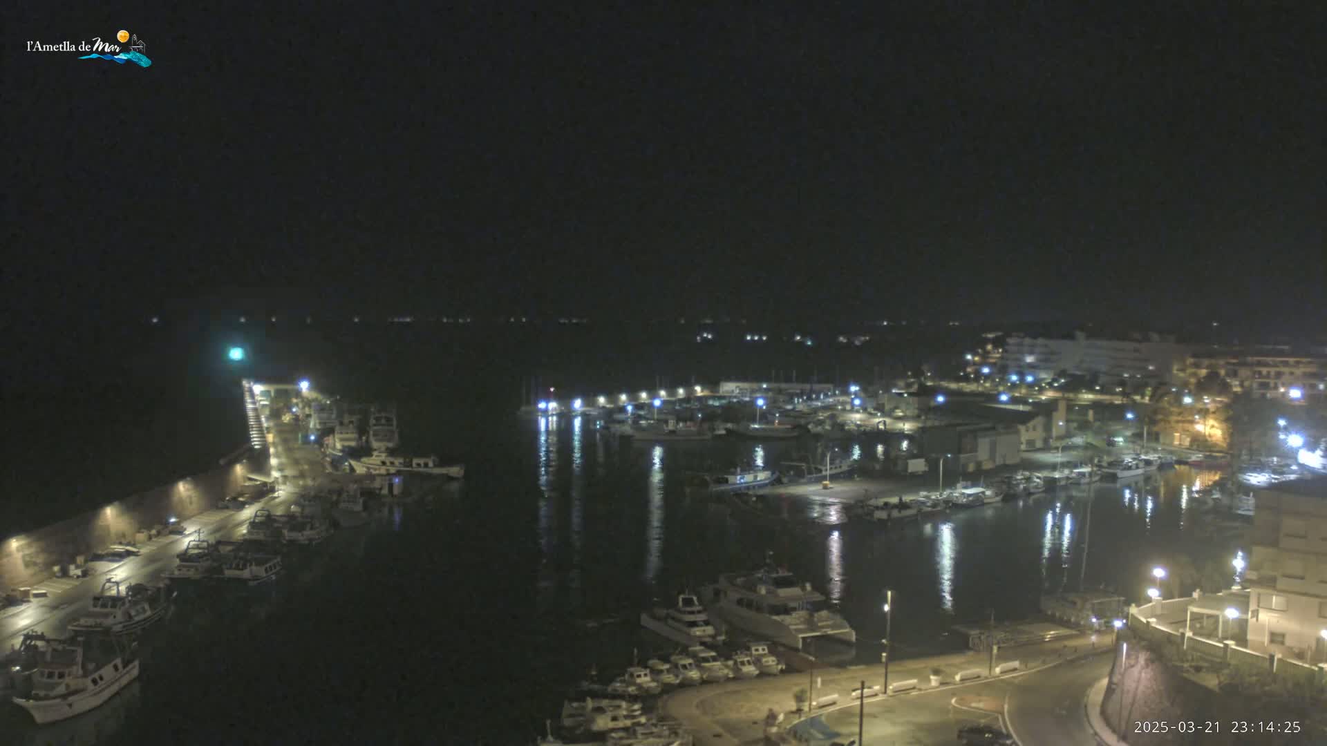 A nighttime view of a harbor filled with boats, illuminated by lights, under a clear, dark sky.