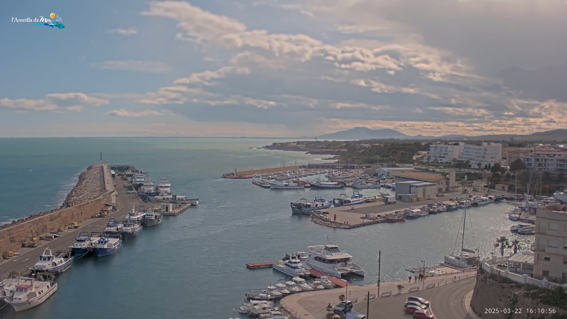 A harbor filled with many boats is shown under a partly cloudy sky.