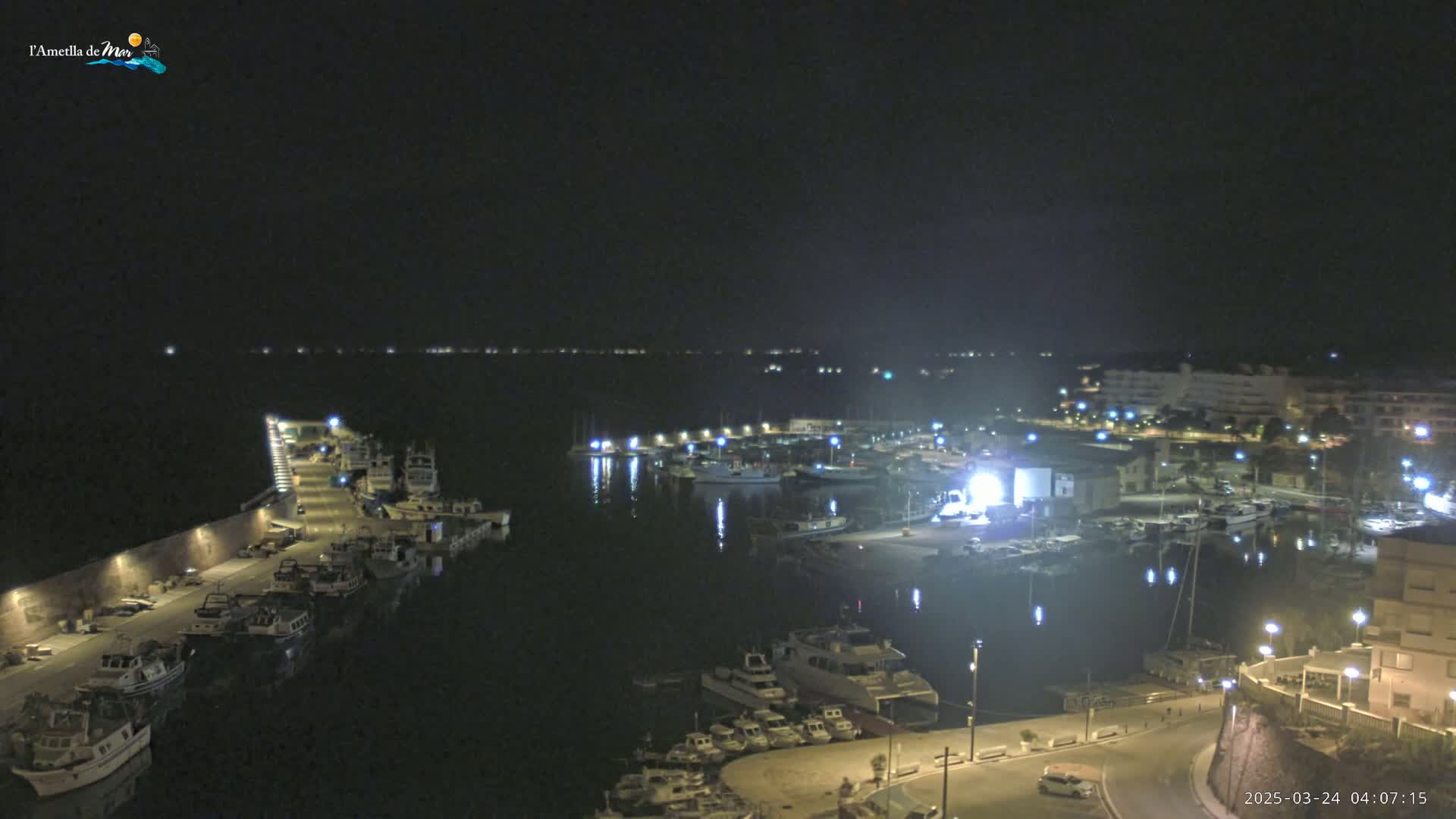 A nighttime view of a harbor filled with boats, illuminated by lights along the docks and buildings in the background.