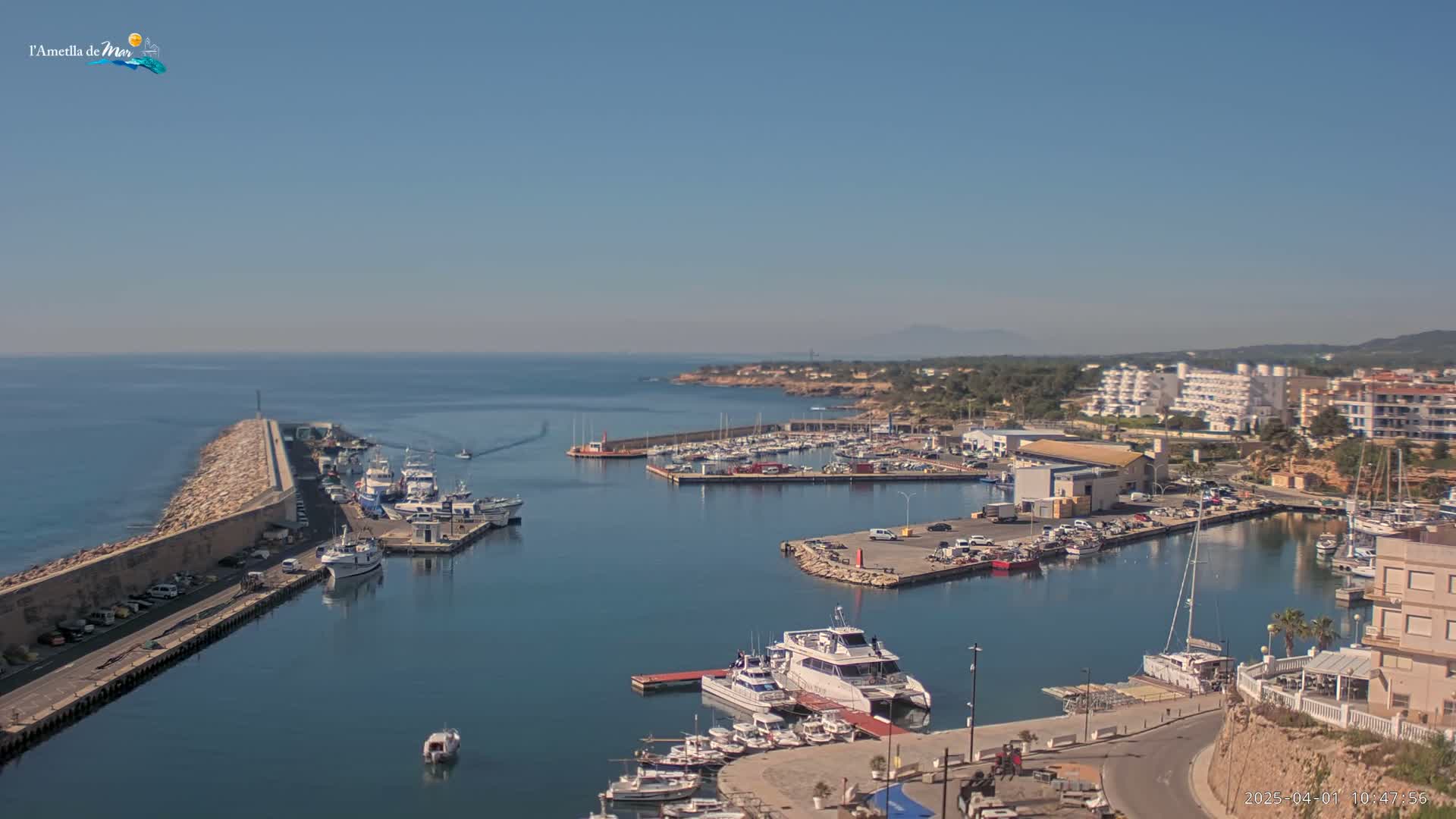 A harbor filled with numerous boats and yachts under a clear blue sky is situated beside a coastal town.