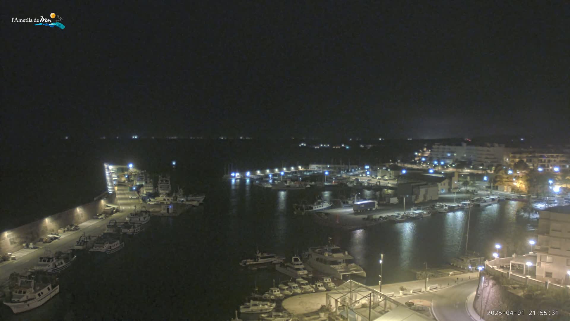 A nighttime, aerial view of a harbor filled with docked boats and surrounded by buildings and lights.