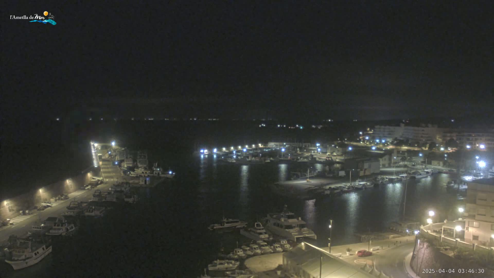 A nighttime aerial view of a harbor filled with boats, illuminated by lights along the docks and surrounding buildings.