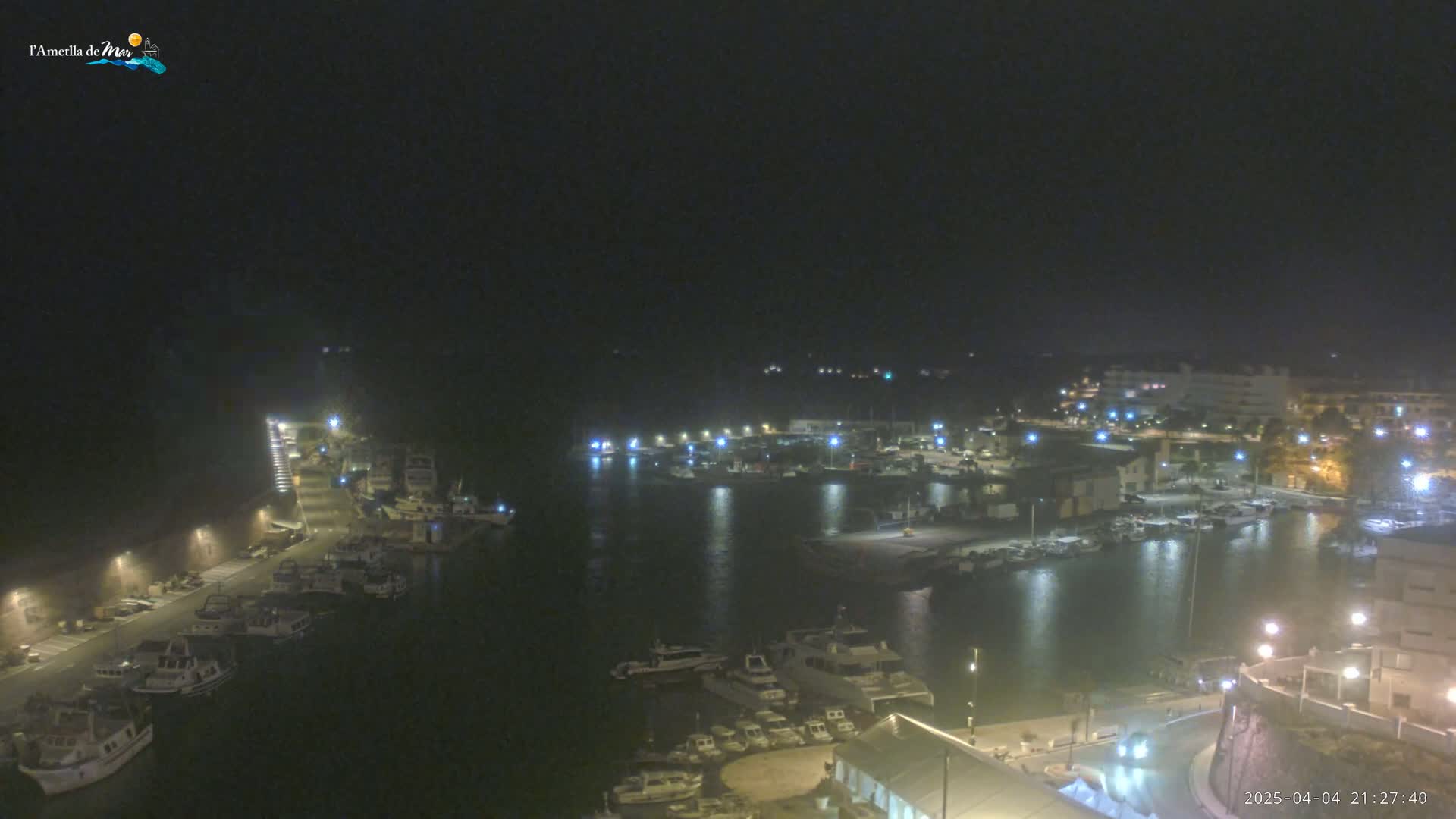 A nighttime, aerial view of a harbor filled with boats, illuminated by streetlights and building lights.