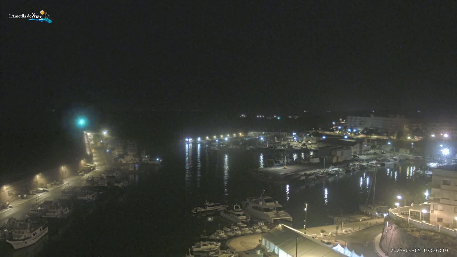 A nighttime, hazy view of a harbor filled with boats, illuminated by lights from buildings and street lamps along the waterfront.