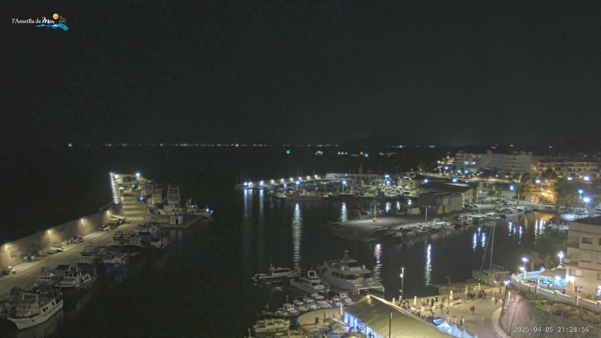 A nighttime harbor filled with boats and illuminated by lights, reflecting on the calm water.