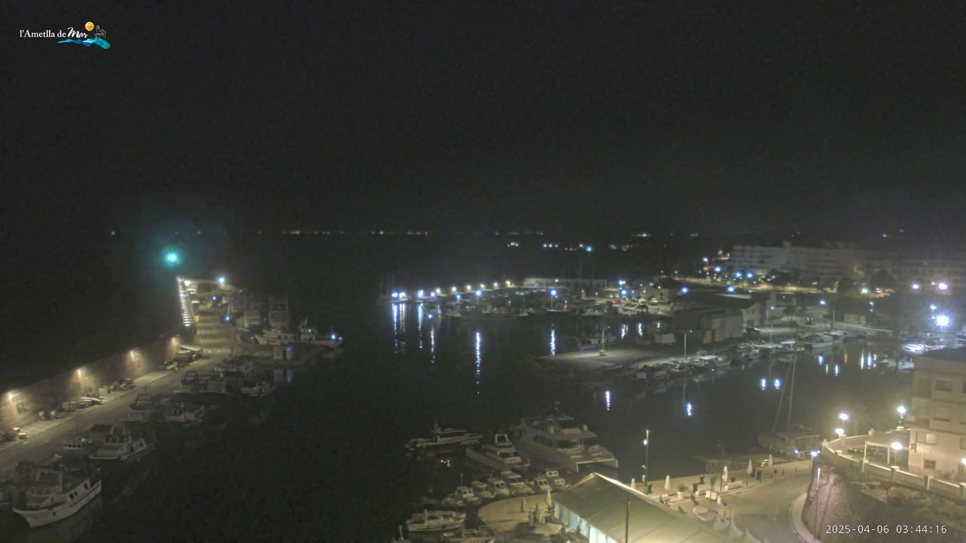 A nighttime, high-angle view of a harbor filled with boats, illuminated by lights along the docks and buildings surrounding the water.