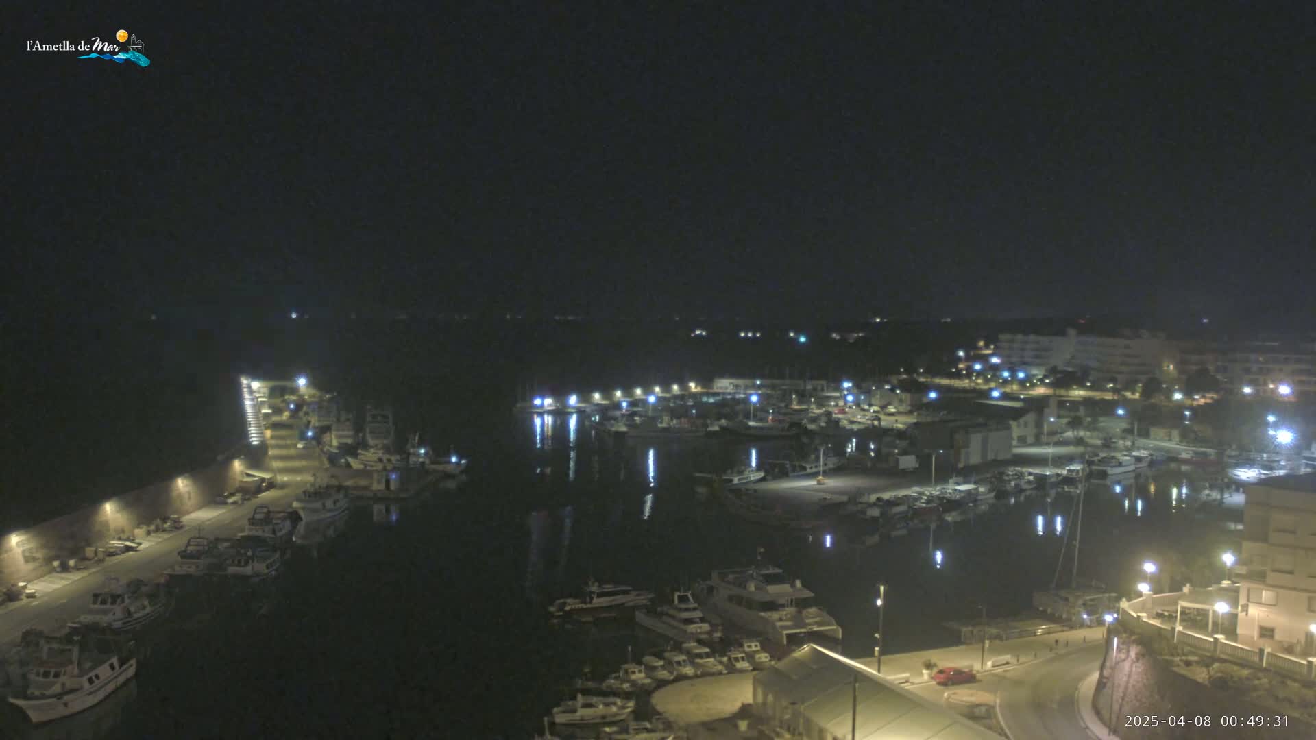 A nighttime aerial view of a harbor filled with boats, illuminated by lights, under a clear, dark sky.