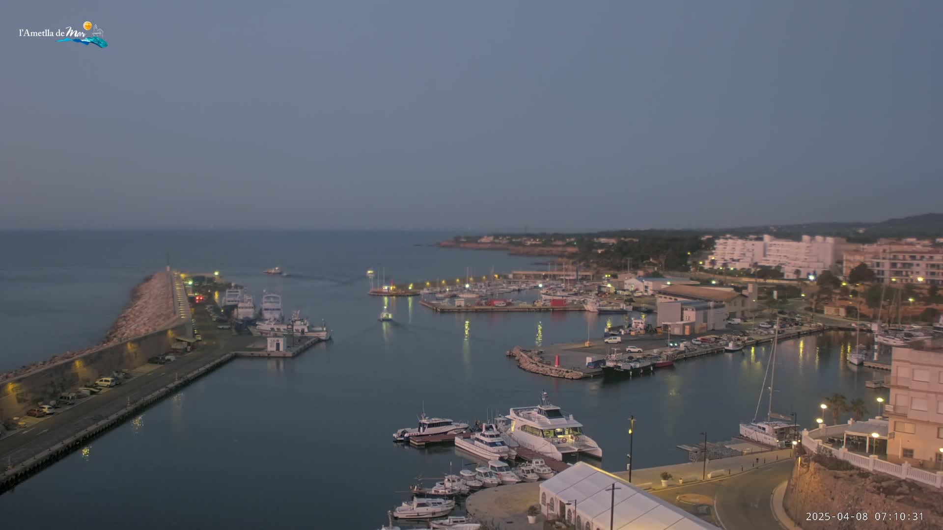 A harbor filled with boats is nestled next to a town at dusk under a clear, dusky sky.