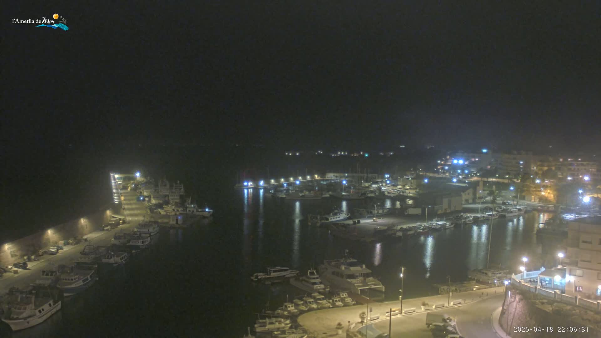 A nighttime, high-angle view of a harbor filled with boats, illuminated by lights from the surrounding buildings and docks.